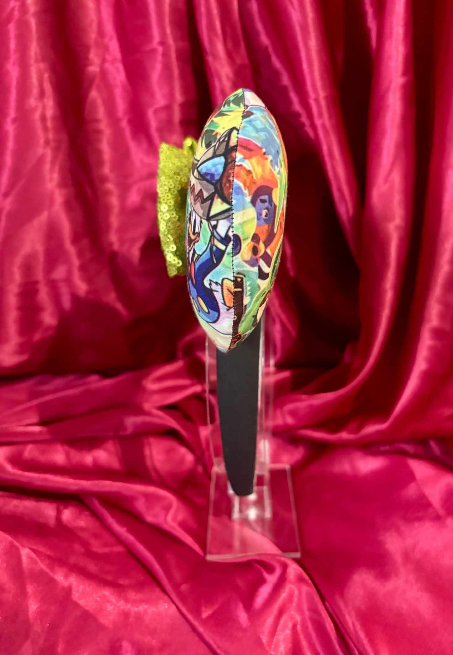 Side view of Colorful Handmade mouse ears with a green bow on a red satin background with duck cartoon images on the ears