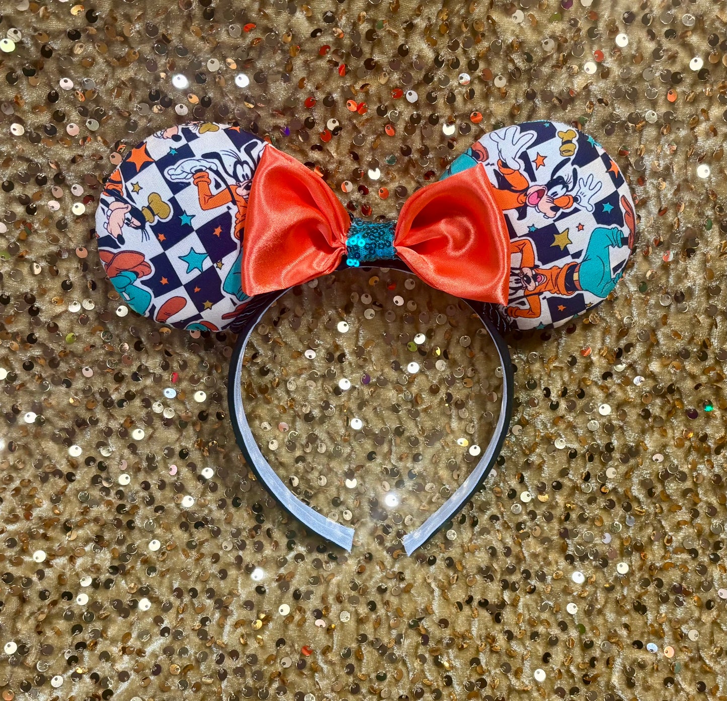 Mouse ears with an orange bow and cartoon character design on a green glittery background