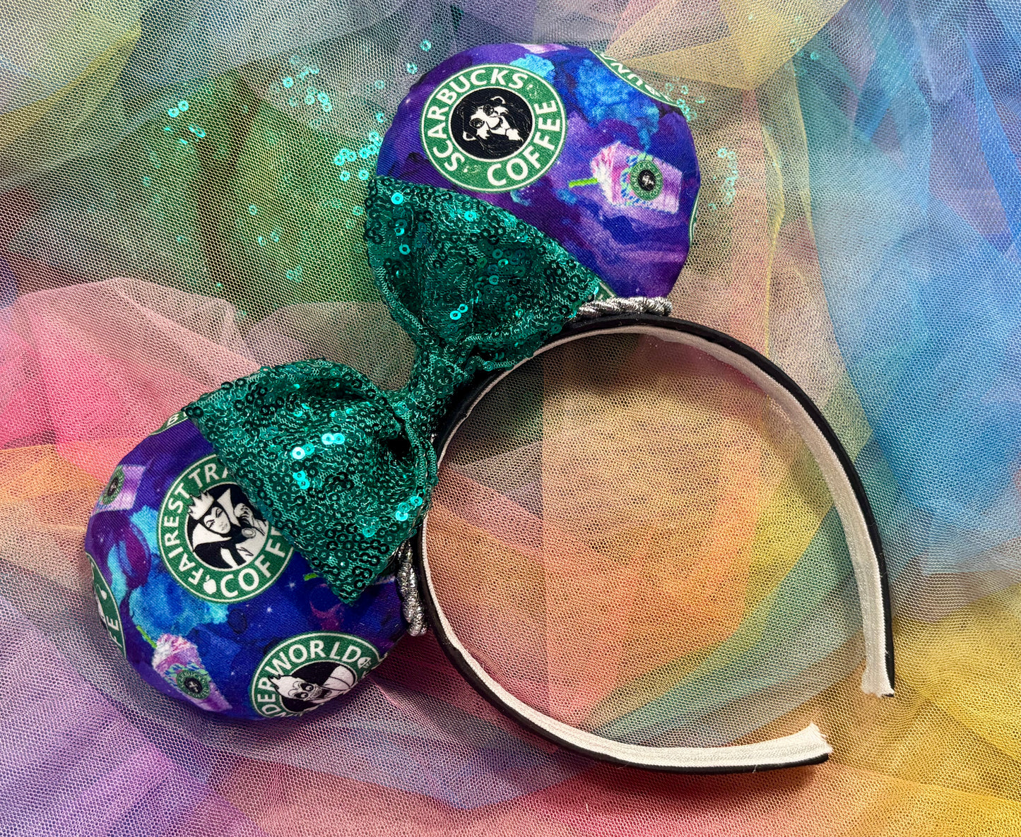 Colorful mouse ears with Coffee logo and villains on the fabric front and back with a teal sequin bow. Shown on a colorful background