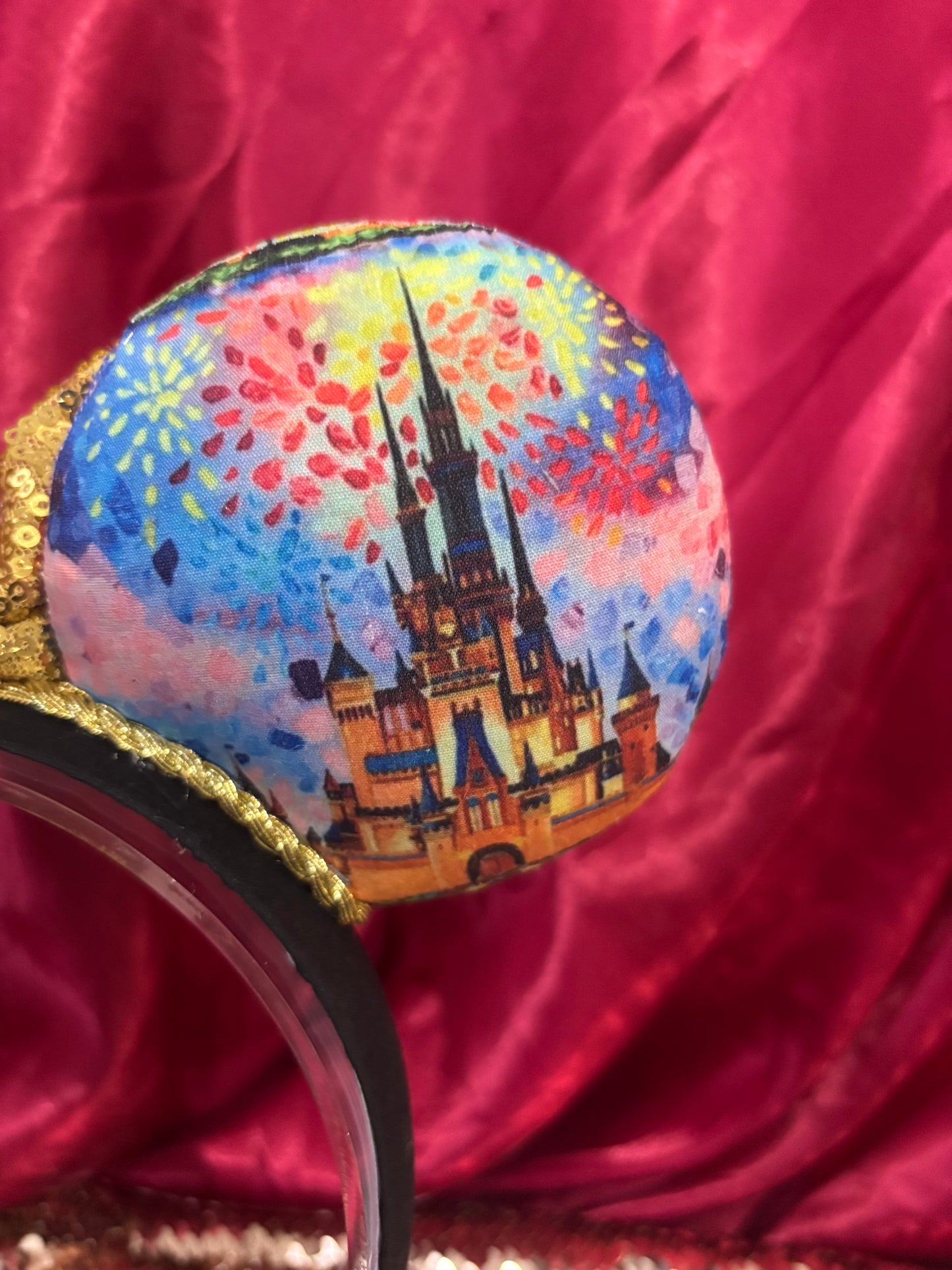 Colorful castle printed mouse ears with a gold sequin bow. Shown on a glittery background