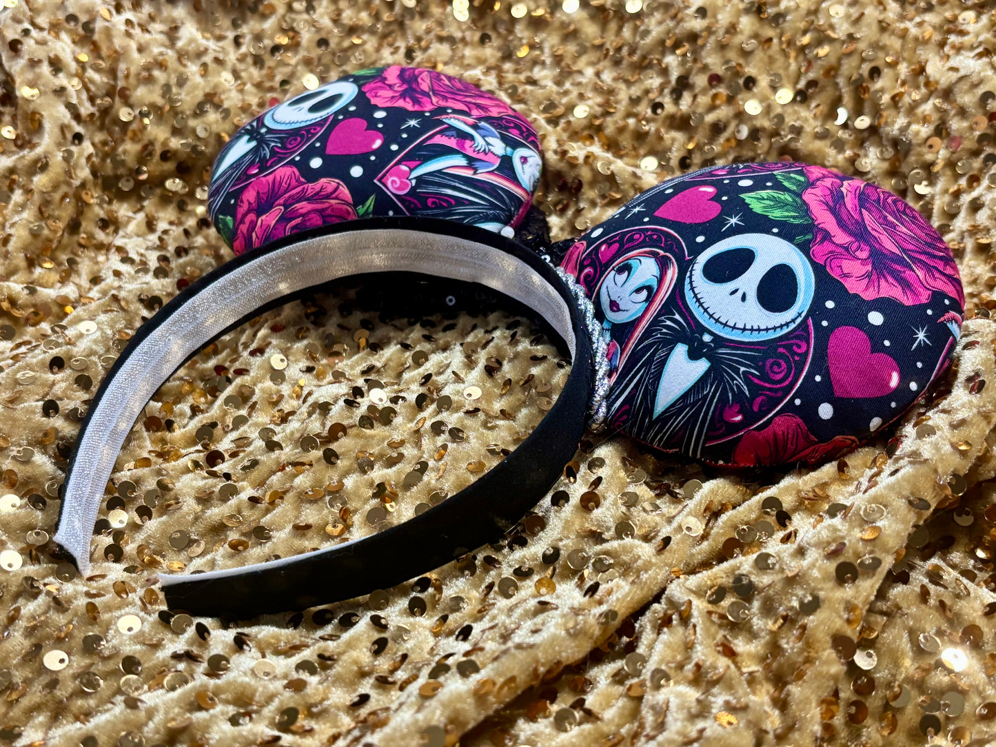 NBC themed mouse ears on a black headband with silver twisted trim and a black sequin bow on a gold sequin background. Back angled view.