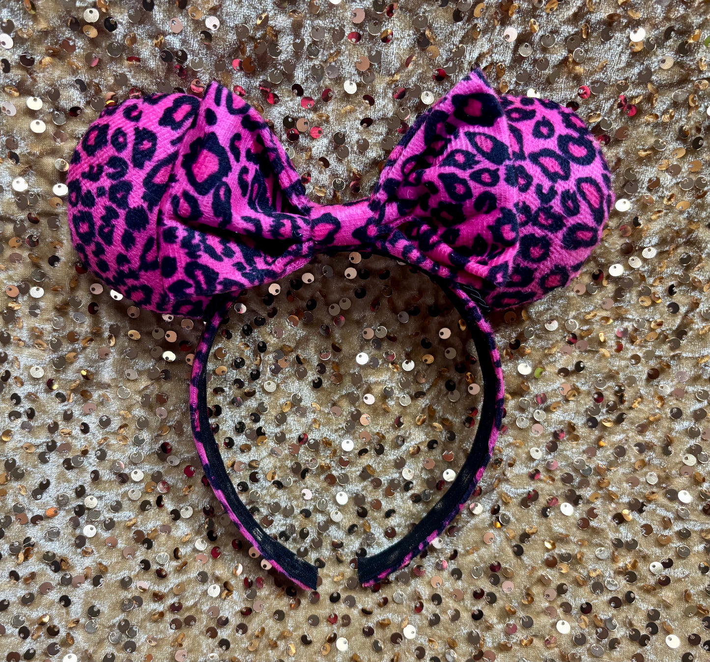 Pink leopard print headband with a bow on a glittery surface