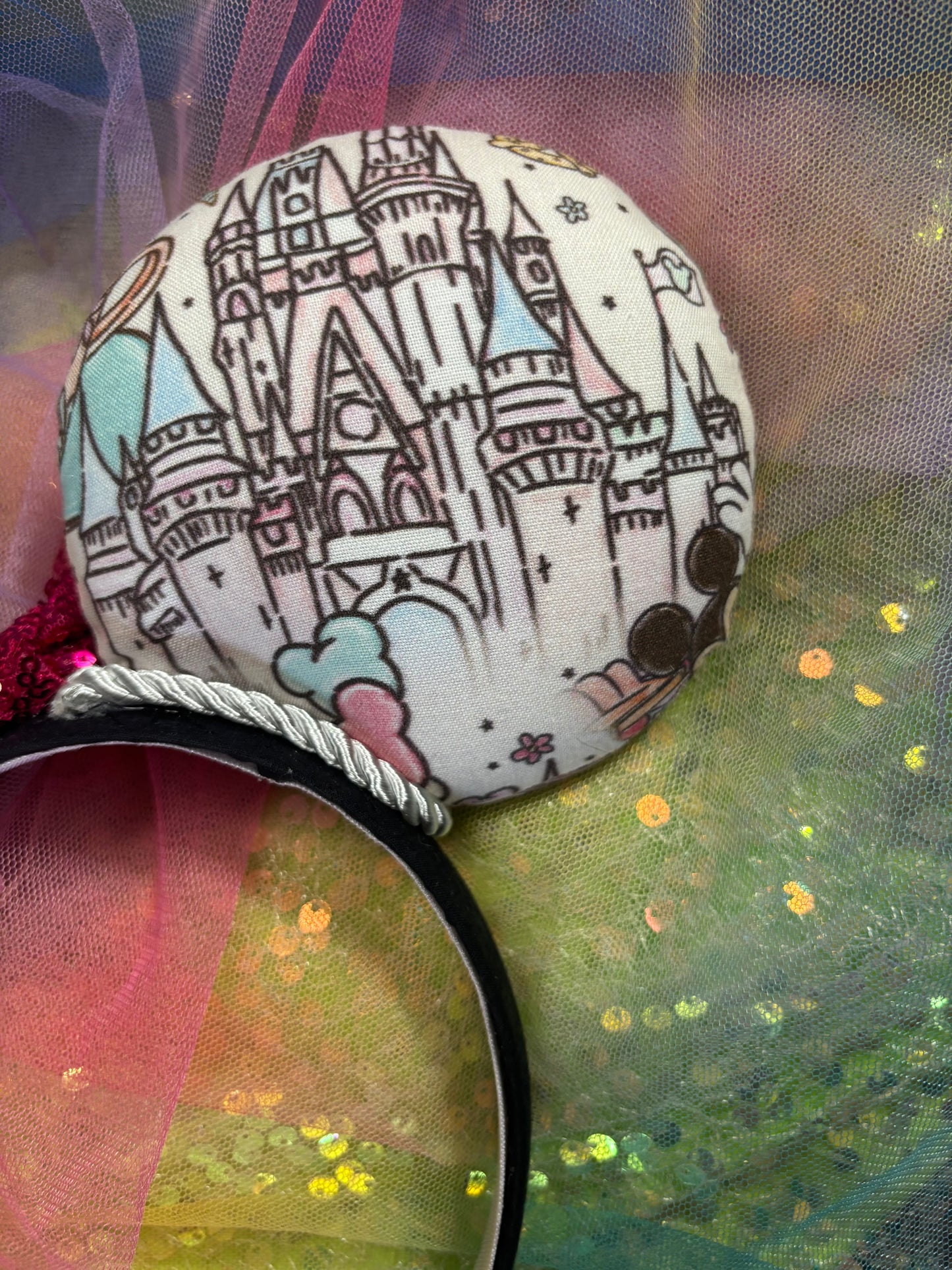 Mouse ears with a colorful design and hot pink sequin bow on a multicolored tulle background
