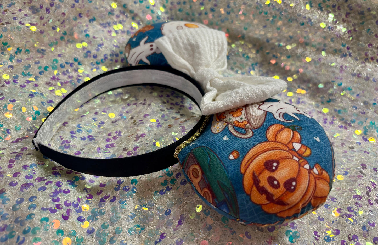 Handmade and ready to ship Fall Mouse ears with pumpkins, eggs, waffles and more shaped like mouse ears is on the front and back of mouse ears with a white waffle print bow on a rainbow glitter background.