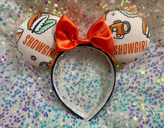 Showgirl themed mouse ears with a orange satin bow on a black headband.