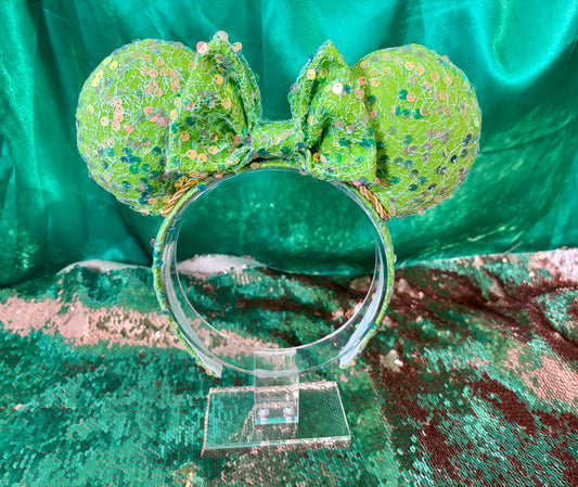 Bright lime Green sequin mouse ears on ears, headband and the bow with a gold trim. Shown on a pastel floral background