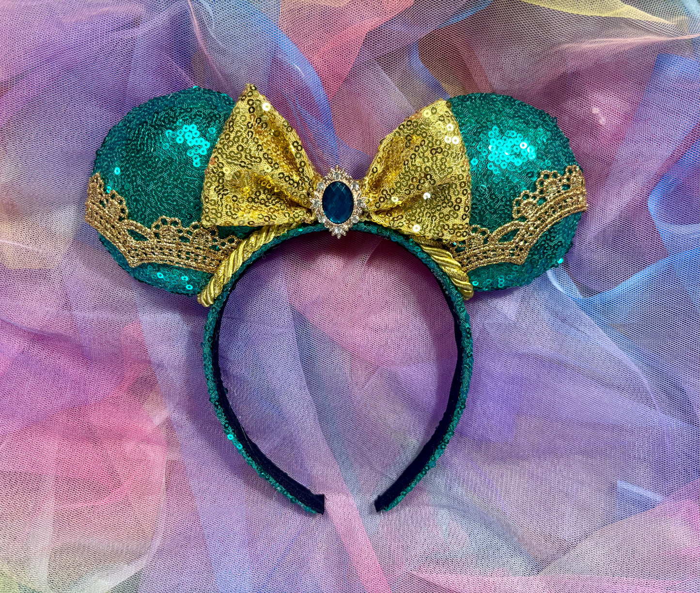 Handmade, and ready to ship. Jasmine inspired Mouse ear headband with teal sequin fabric on the front and back of ears with a gold sequin bow with a teal embellishment in the middle of bow. gold along the ears and the trim as well. Mouse ears are on a Universal sized headband that also has teal on it.