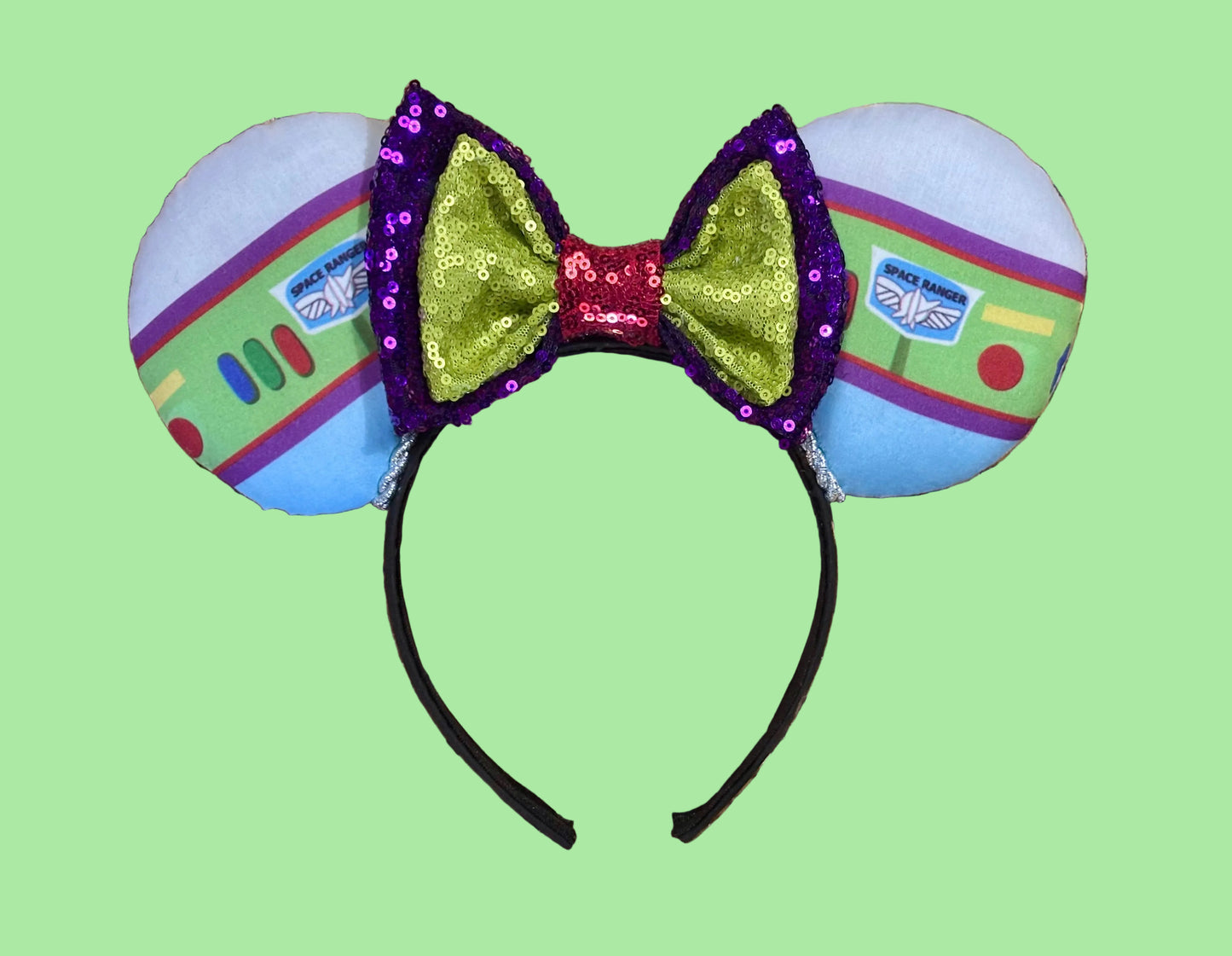 Space Ranger Mouse Ear headband with new improved bow. Handmade and ready to ship with Space ranger fabric on both the front and the back of mouse ears. The set has a silver twisted trim along the inner ears and a new sequin bow that is purple, lime green and red in sequin. Ears are on a black poly cotton universal sized headband.