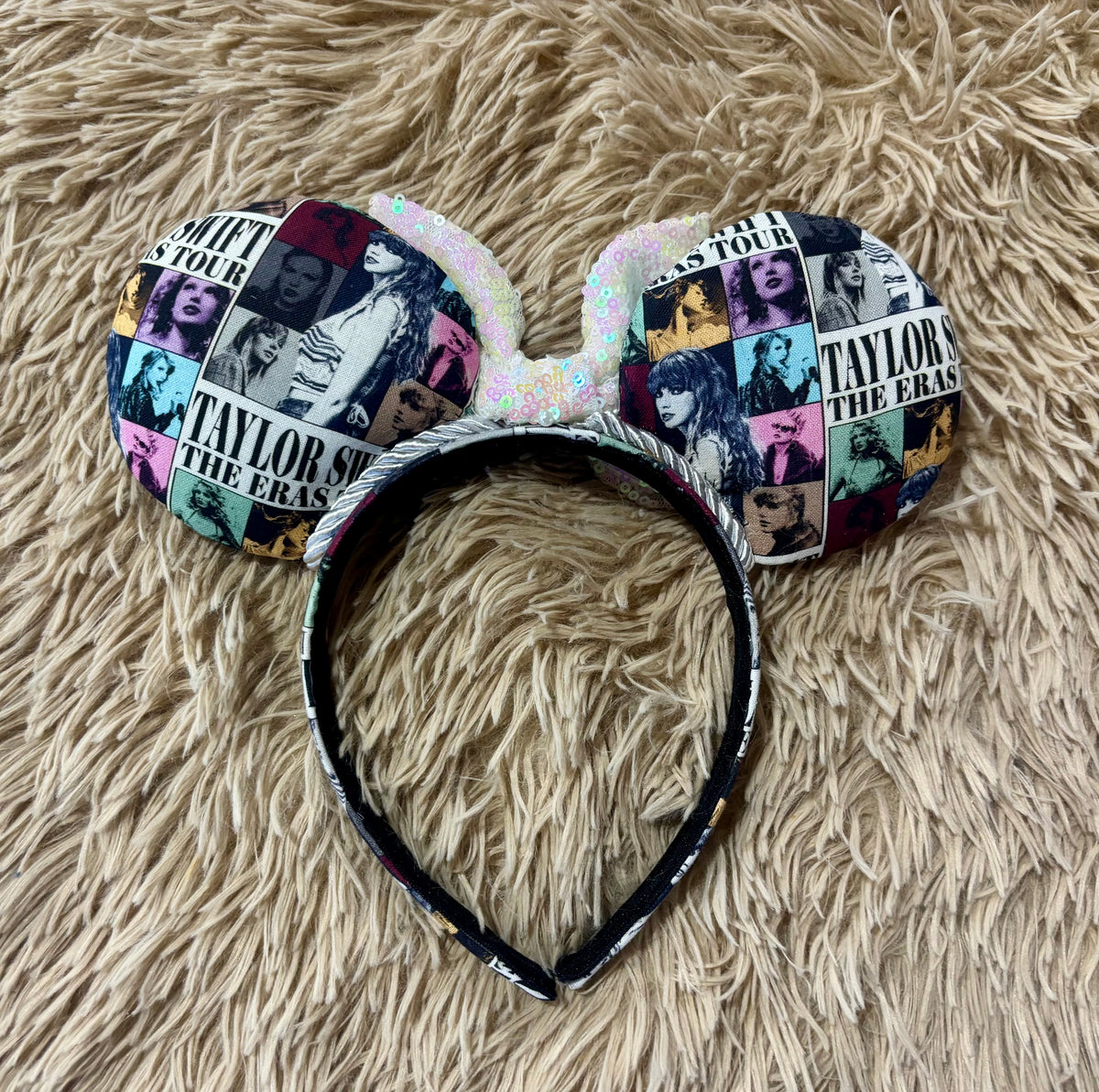 Back view of ear headband featuring a collage print do album art, displayed on a beige shag rug. The headband has the same fabric with silver trim, and the ears have a iridescent bow.