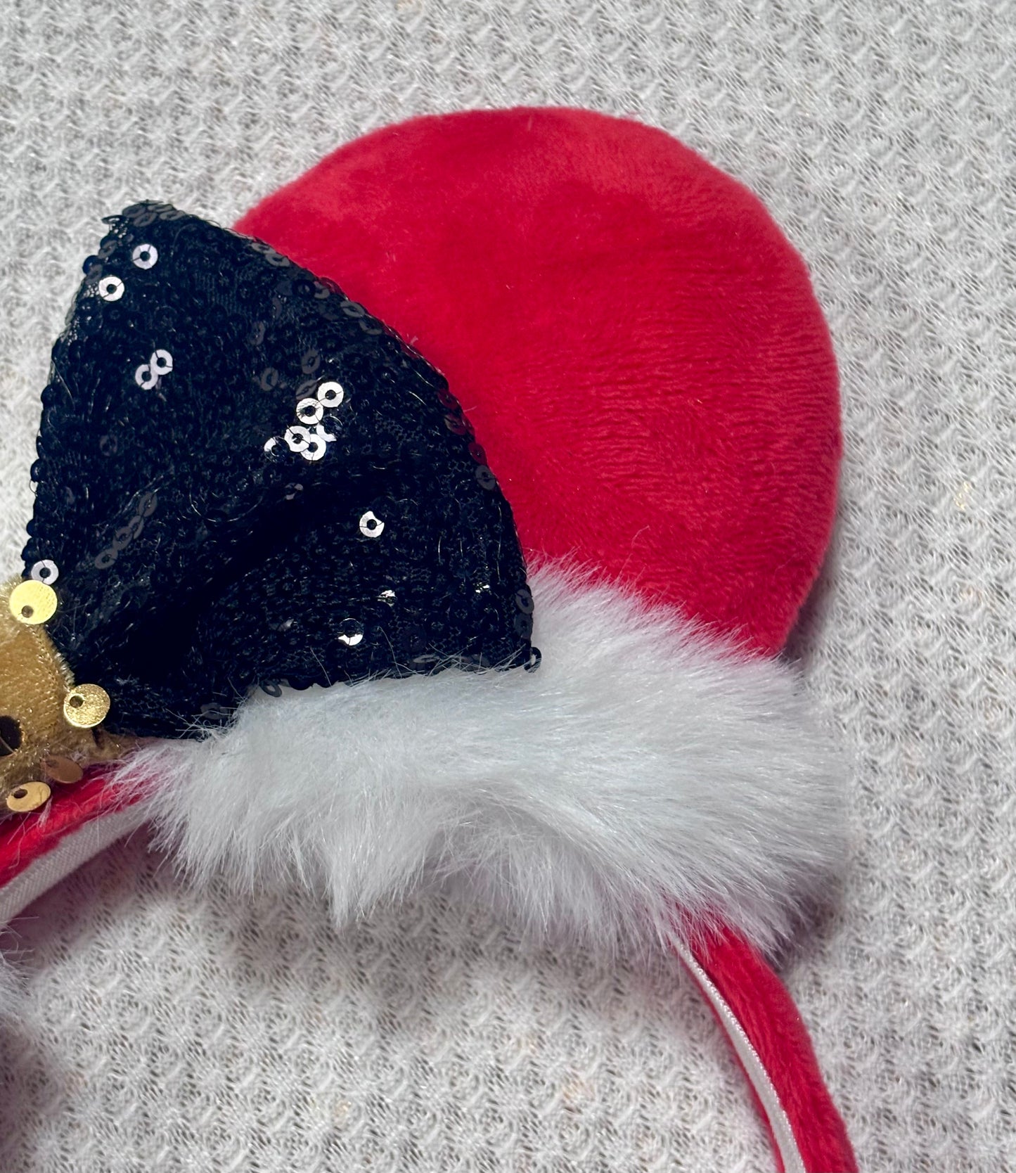 Minnie Mouse ears headband with red plush ears and black bow with gold middle and fluffy white trim on a white background