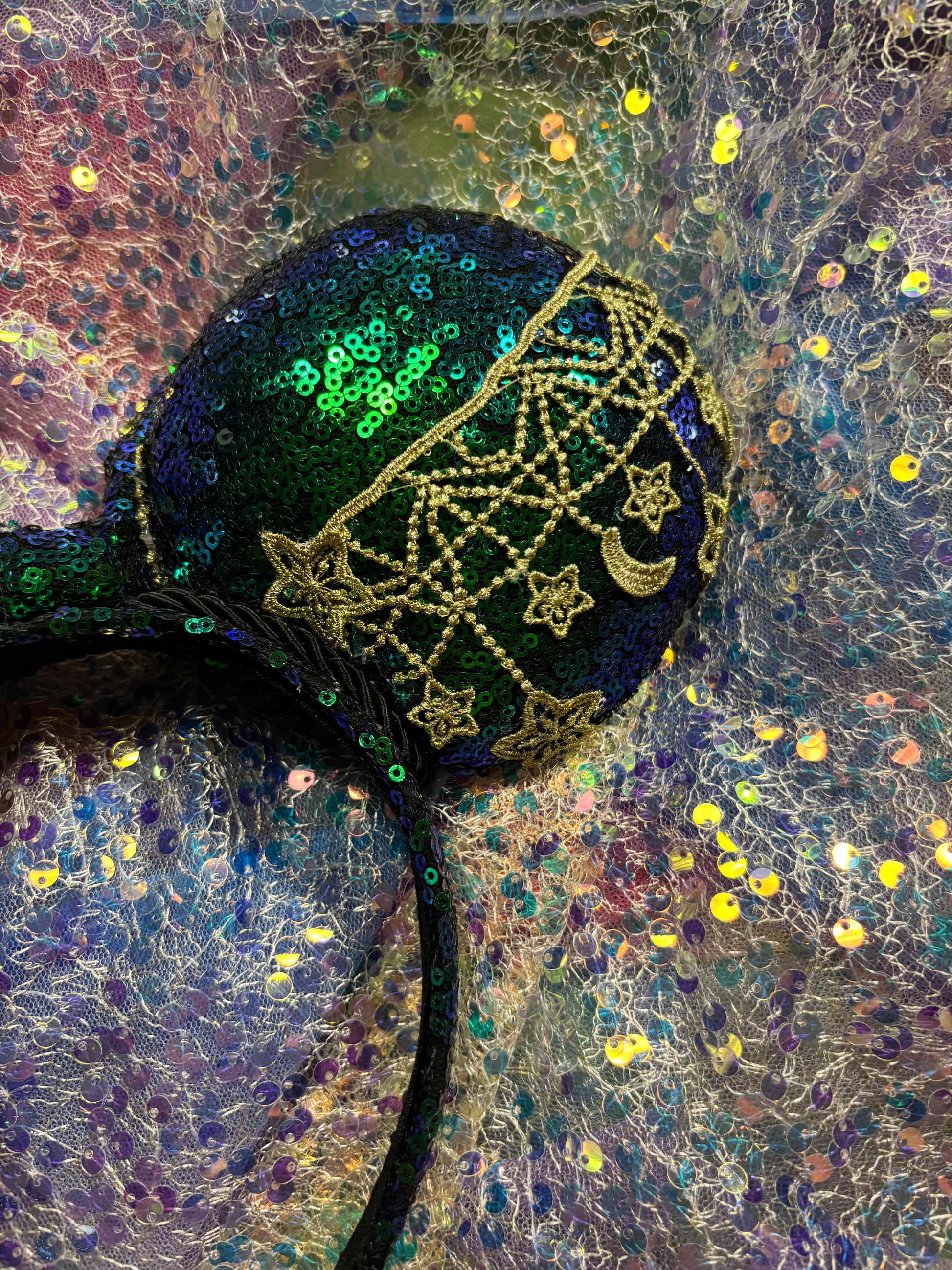 Mouse Ear headband that is a Handmade Iridescent blue and green sequins with gold sun, moon and stars attached to them. bow with star and moon patterns on a glittery background.
