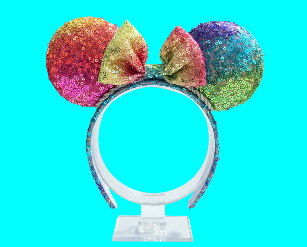 Handmade and ready to ship. Mouse ears with rainbow fabric are on the front and back of mouse ears along with the headband with a matching rainbow sequin bow. Shown on a white background.