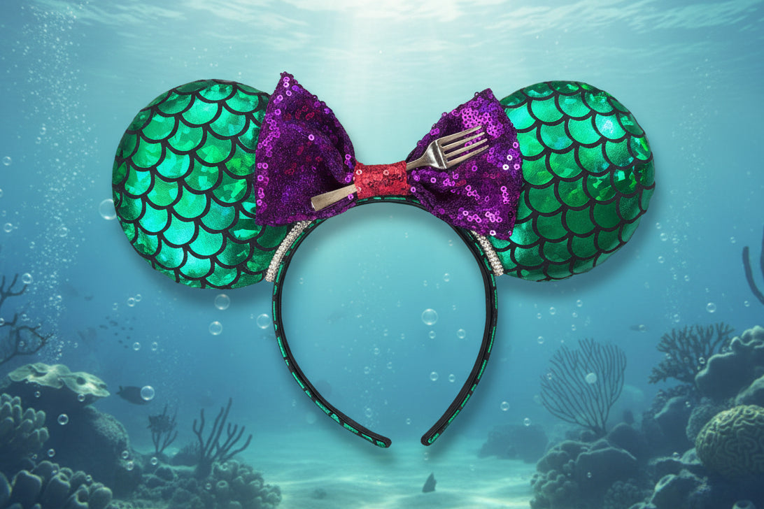 Mermaid-themed mouse ear headband with green scales and purple bow with a dinglehopper in the middle. Shown on a blue underwater background