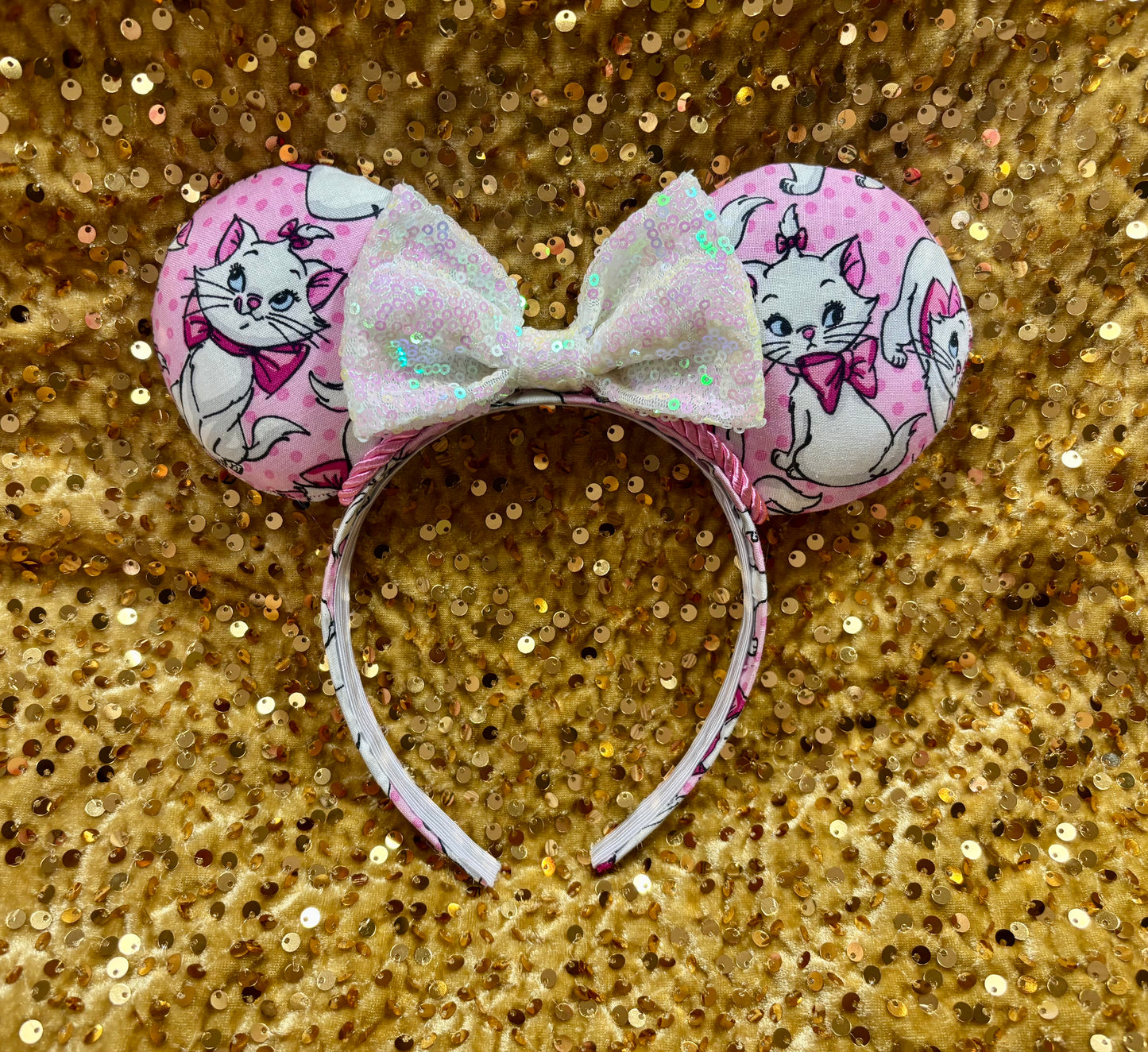 Pink mouse ear headband with white bow shown on a gold glitter background