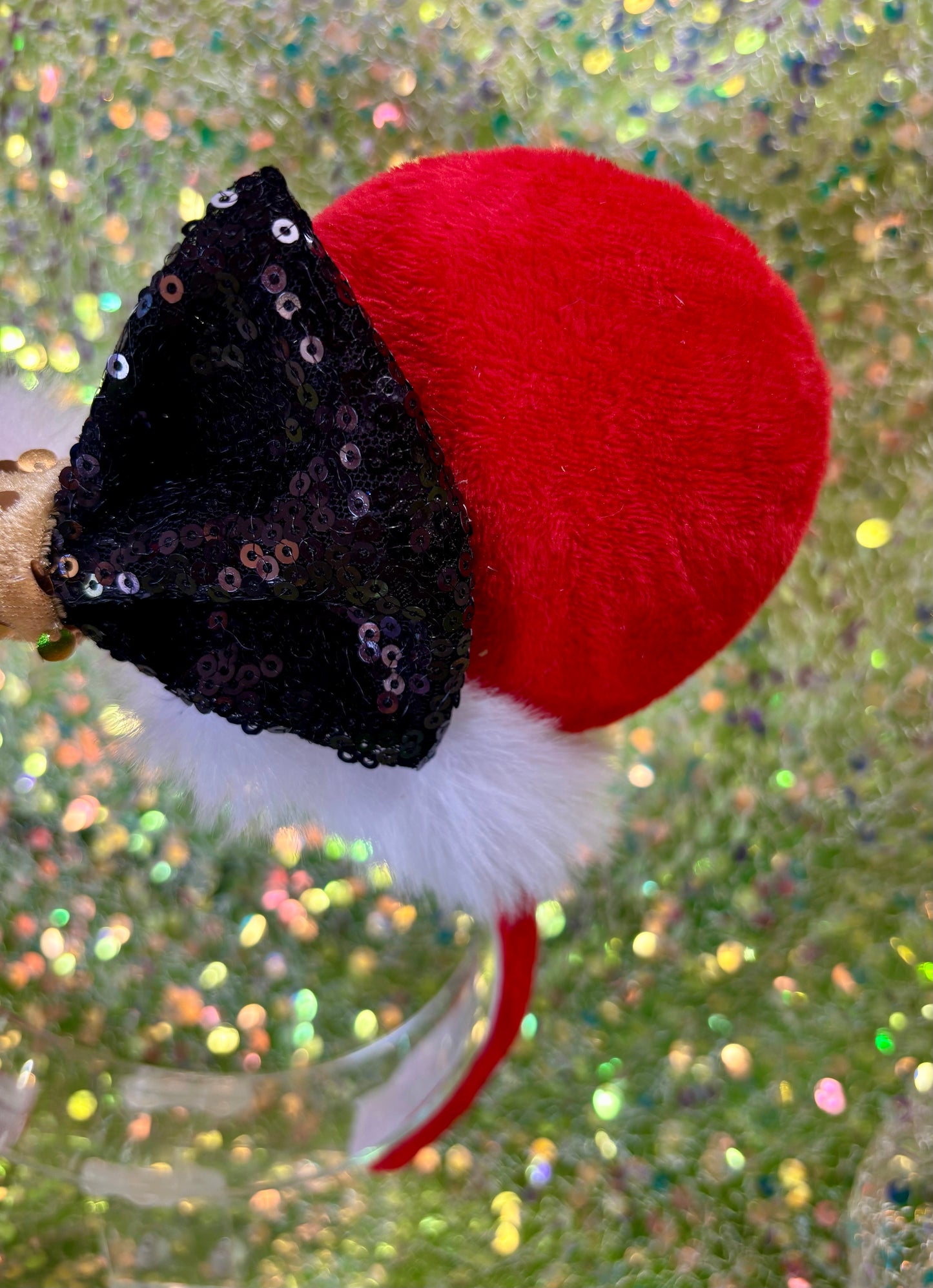 Minnie Mouse ears headband with red plush ears and black bow with gold middle and fluffy white trim on a glitter background