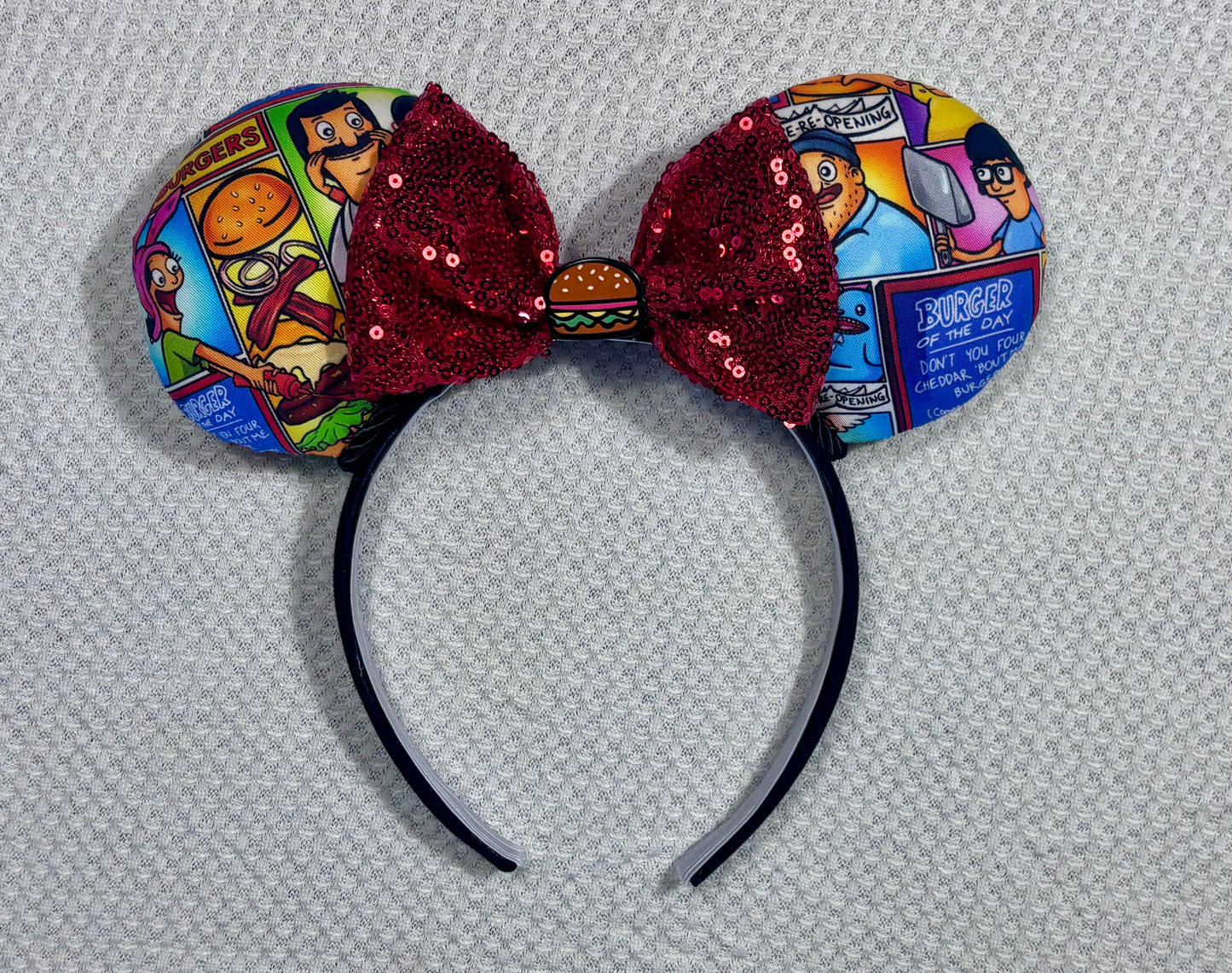 Handmade and ready to ship Belcher and friends mouse ears with the fabric on both the front and back. The headband is black universal sized and fits most. The set has a red sequin bow with a burger embellishment on the middle. Item is shown on a white background.