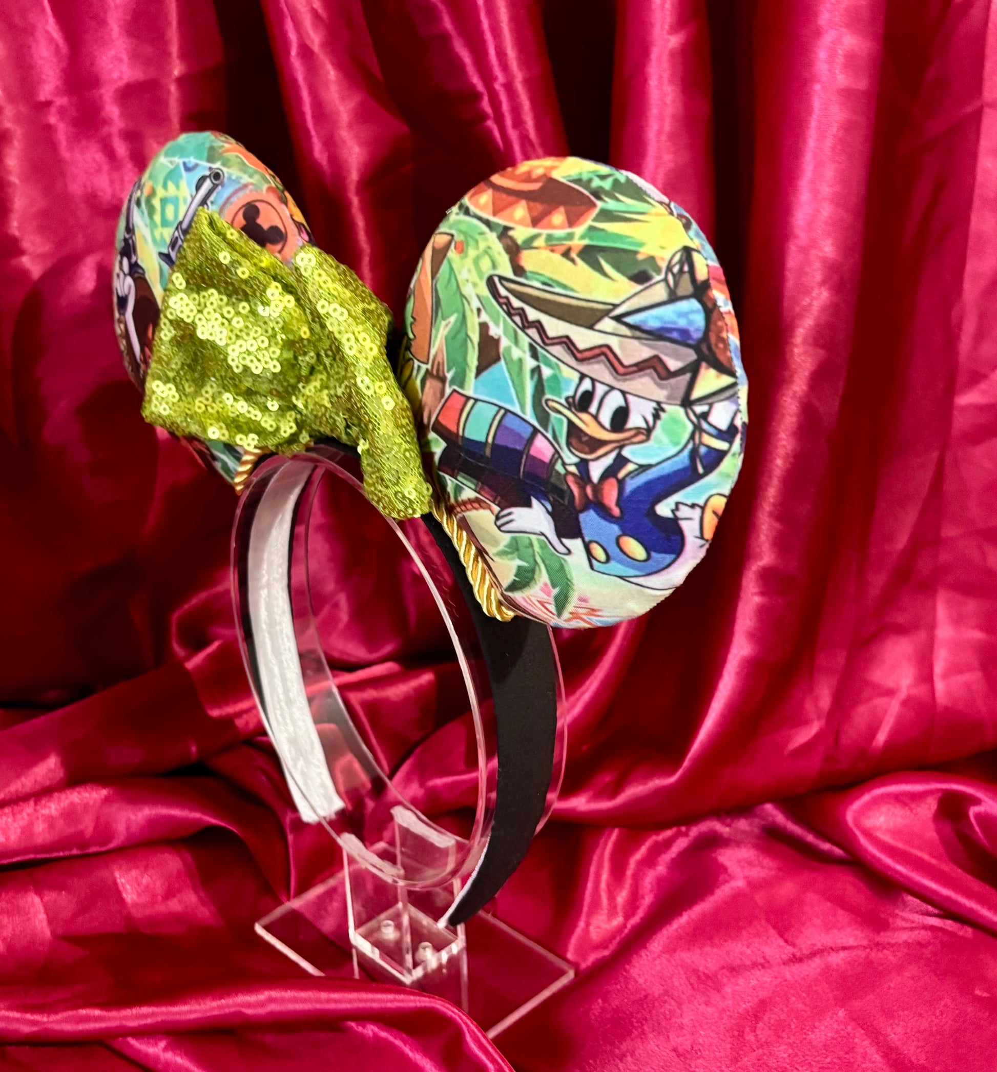 angled side view of Colorful Handmade mouse ears with a green bow on a red satin background with duck cartoon images on the ears