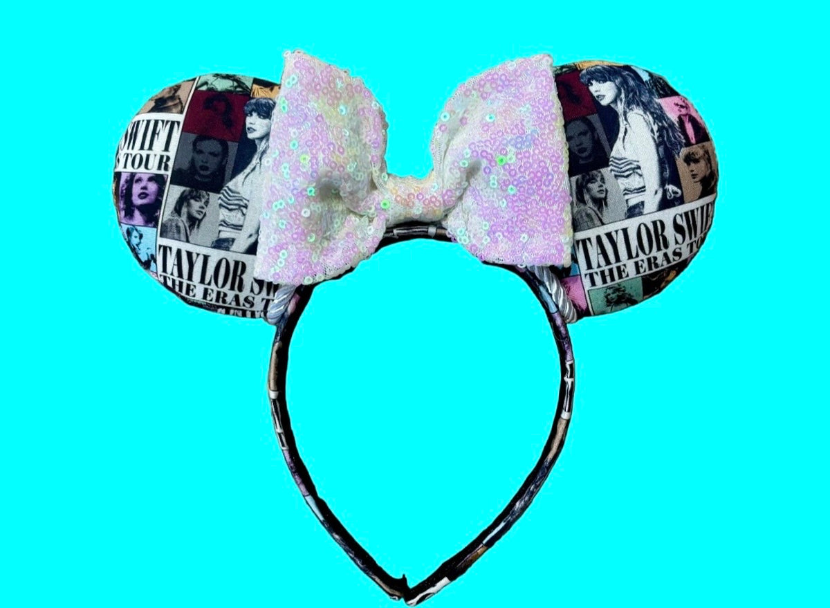 A custom ear headband featuring round ears covered in a black-and-white collage print with 'TS The Eras', topped with a large iridescent white sequined bow, set against a solid bright background.