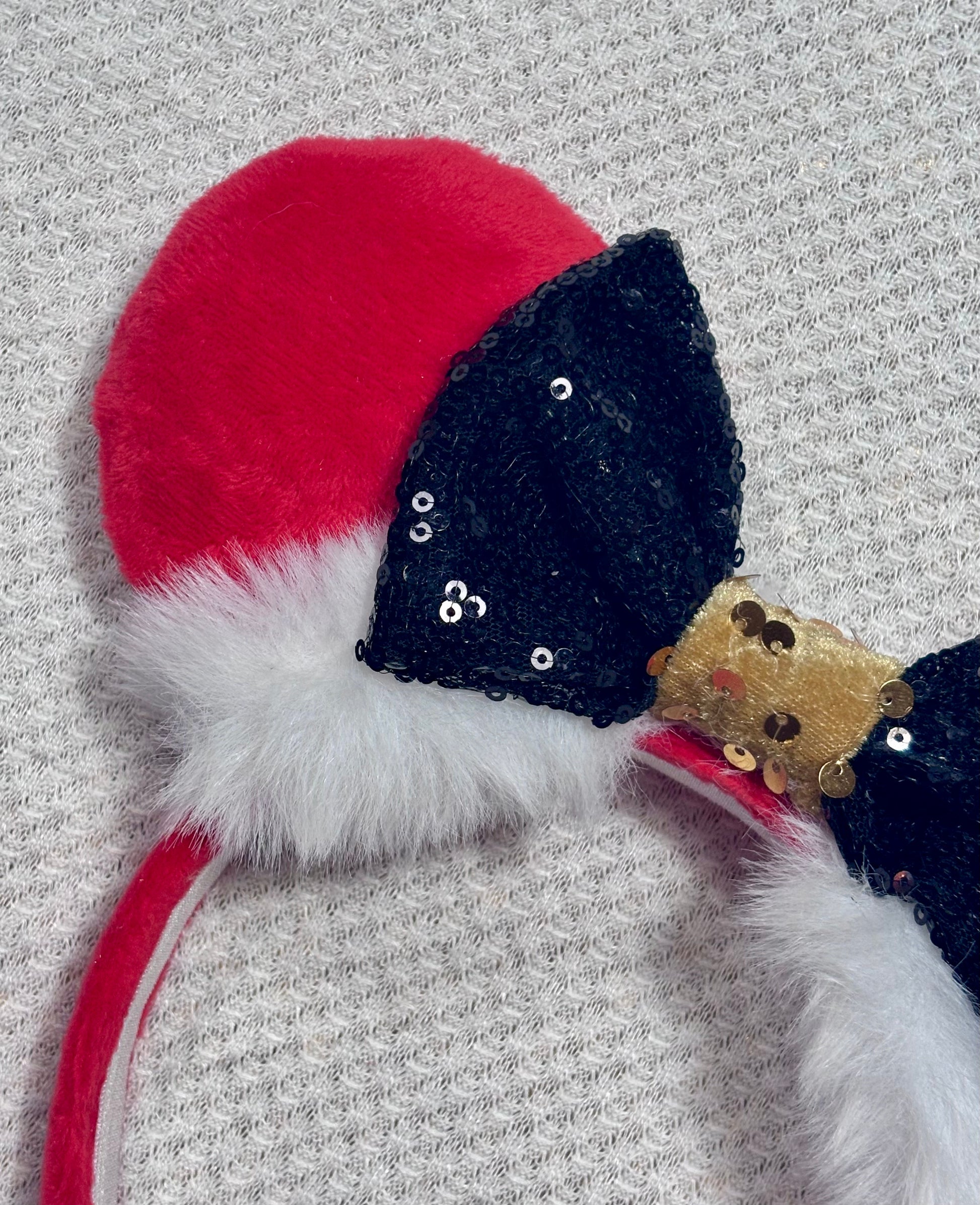 Minnie Mouse ears headband with red plush ears and black bow with gold middle and fluffy white trim on a white background