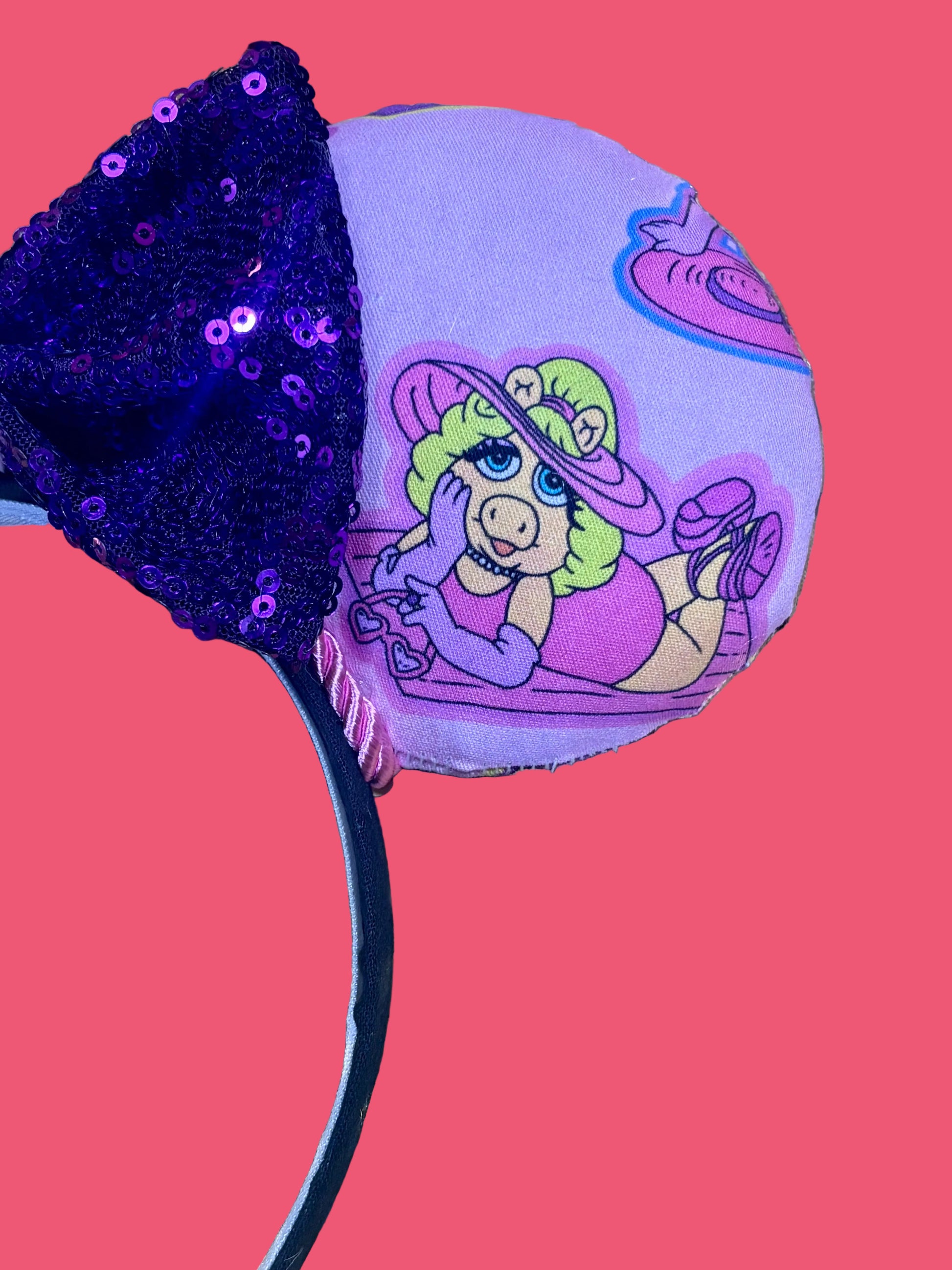 Handmade and ready to ship Piggy mouse ears. Miss Piggy fabric is on the front and the back. On a universal sized black poly fabric headband. With a purple sequin with pink soft middle on the bow.  Right front side of mouse ear view.