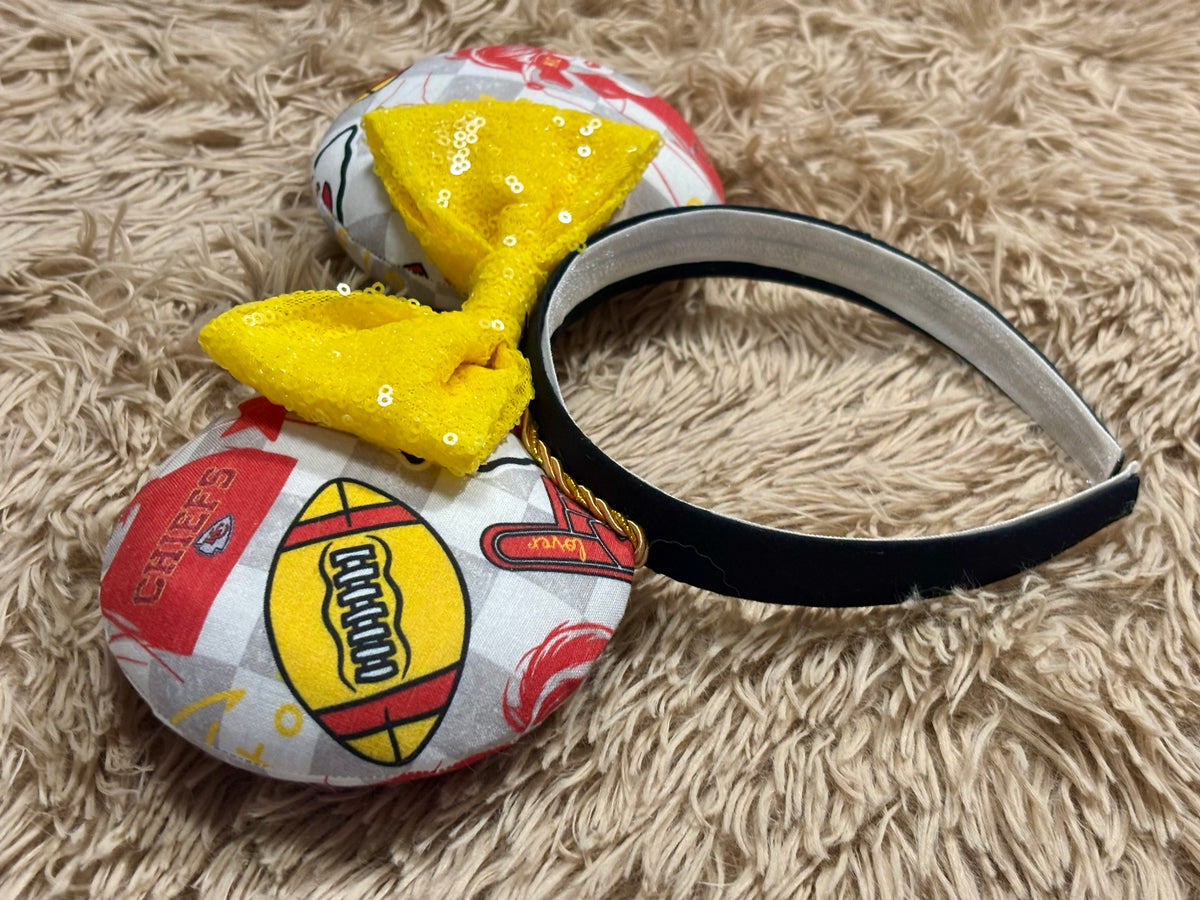 An ear headband featuring a bright yellow sequined bow. The set has TS and Chiefs images on it. Set on a universal sized headband.