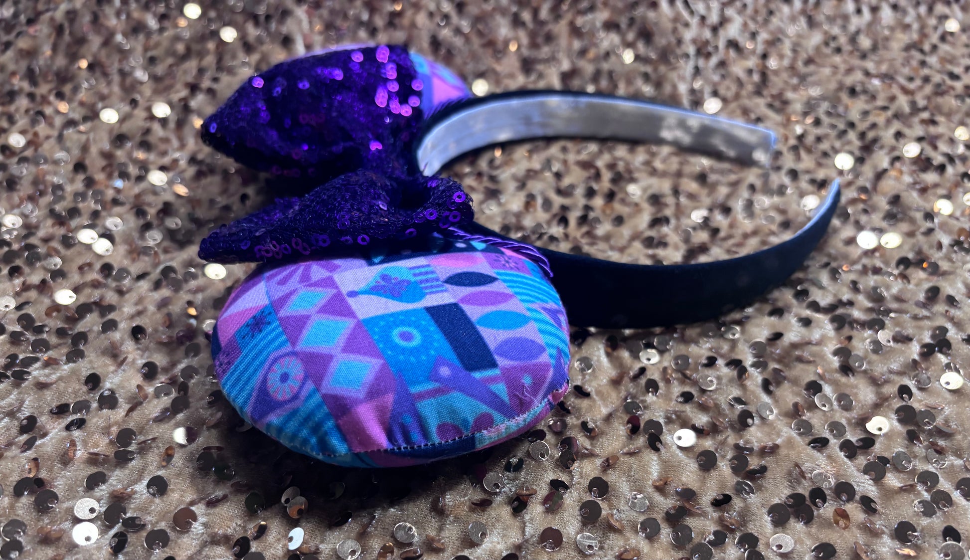 Decorative headband with purple, pink and blue pattern on a glittery surface