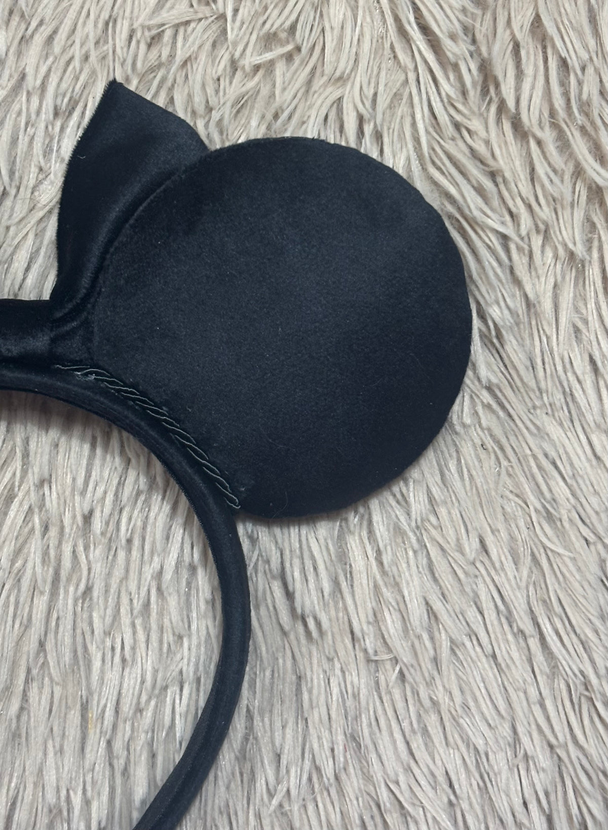 Black velvet ears headband laid on a textured beige faux fur surface.