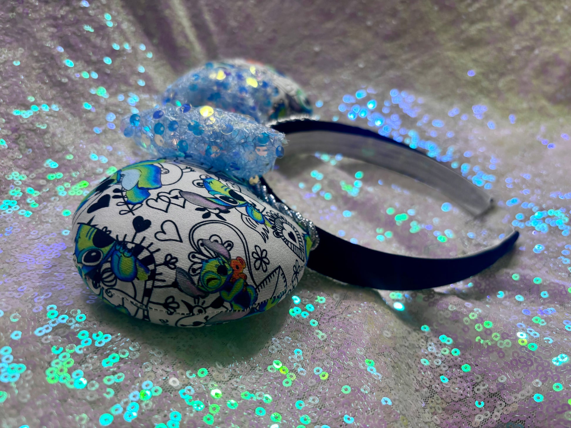 The side view of mouse ears. Handmade and ready to ship Mouse ears with Stitch cartoon character design on the fabric with silver twisted trim on a black universal sized headband and a blue sequin bow.