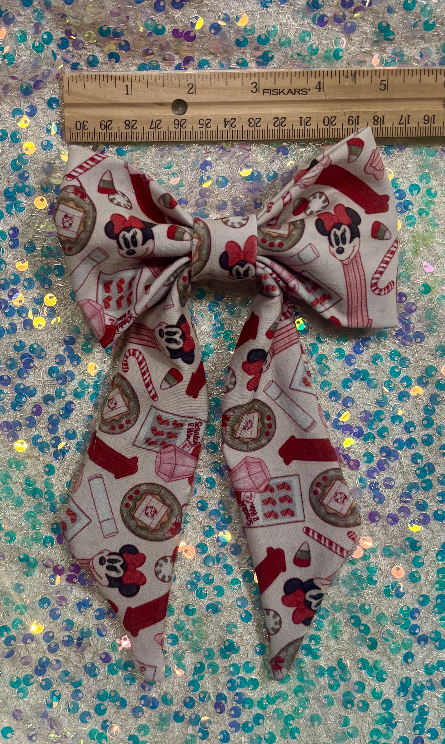 Christmas Stocking Stuffers bow with a ruler for scale on a glittery background. 