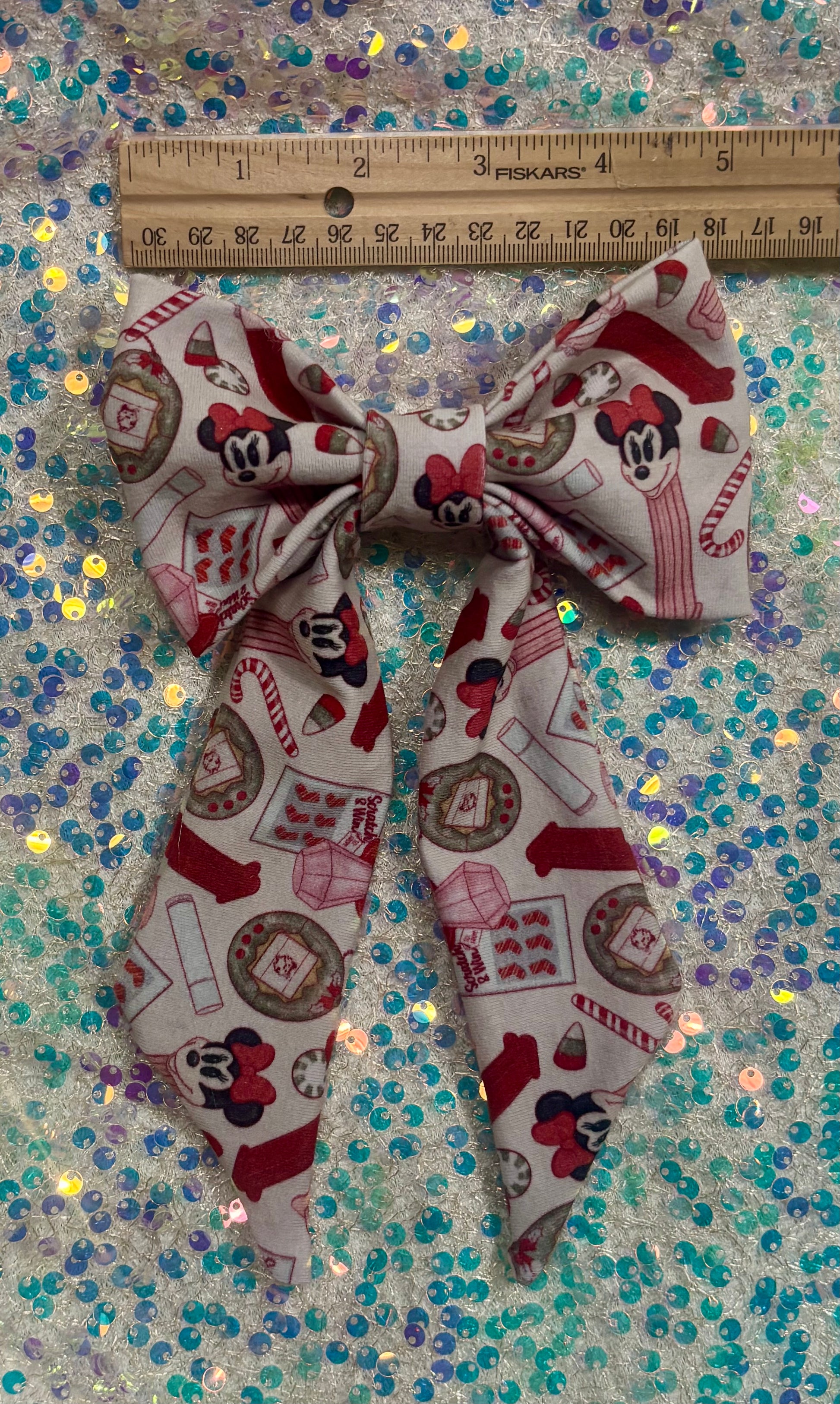 Christmas Stocking Stuffers bow with a ruler for scale on a glittery background. 