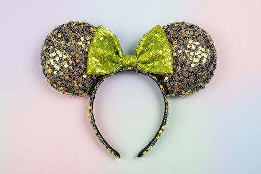 Sparkly black iridescent mouse ears with a lime green sequin bow with black twisted trim on a colorful fabric background.