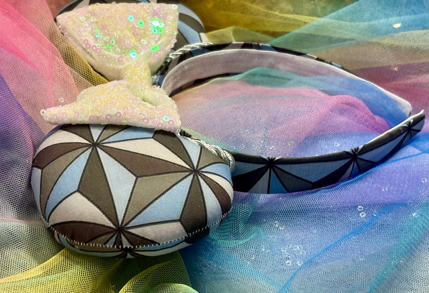 Decorative headband with geometric pattern representing Epcot on a colorful fabric background. Showing the side view of ear.