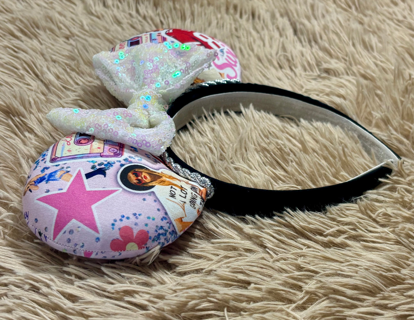 An ear headband with a large iridescent bow and custom printed ears featuring retro cassette graphics, a pink star, and a portrait of singer.