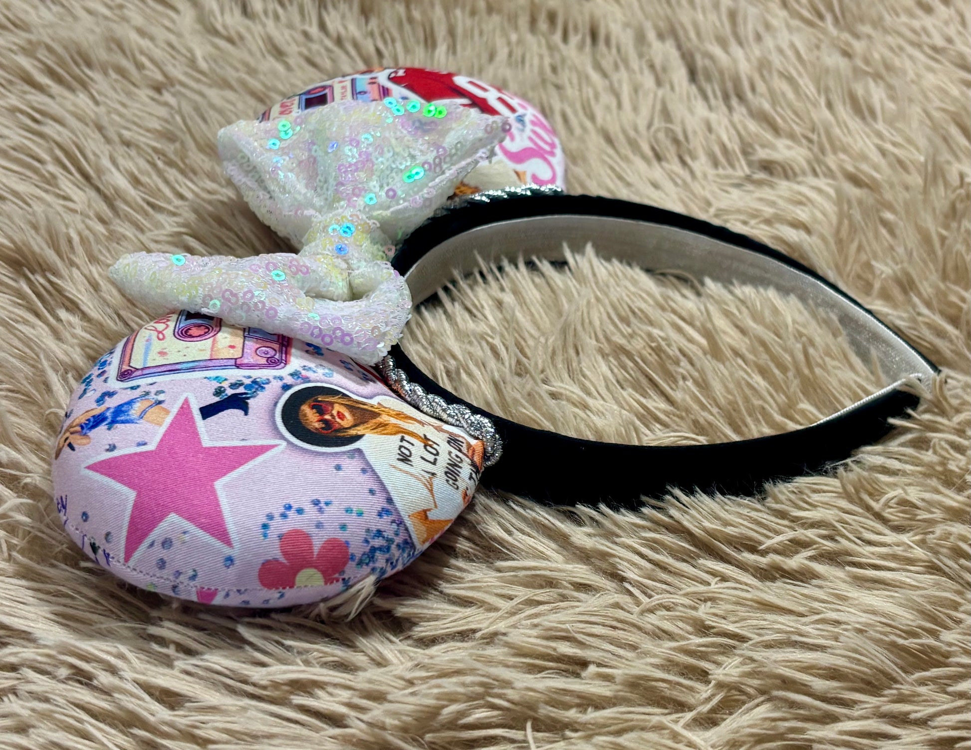 An ear headband with a large iridescent bow and custom printed ears featuring retro cassette graphics, a pink star, and a portrait of singer.