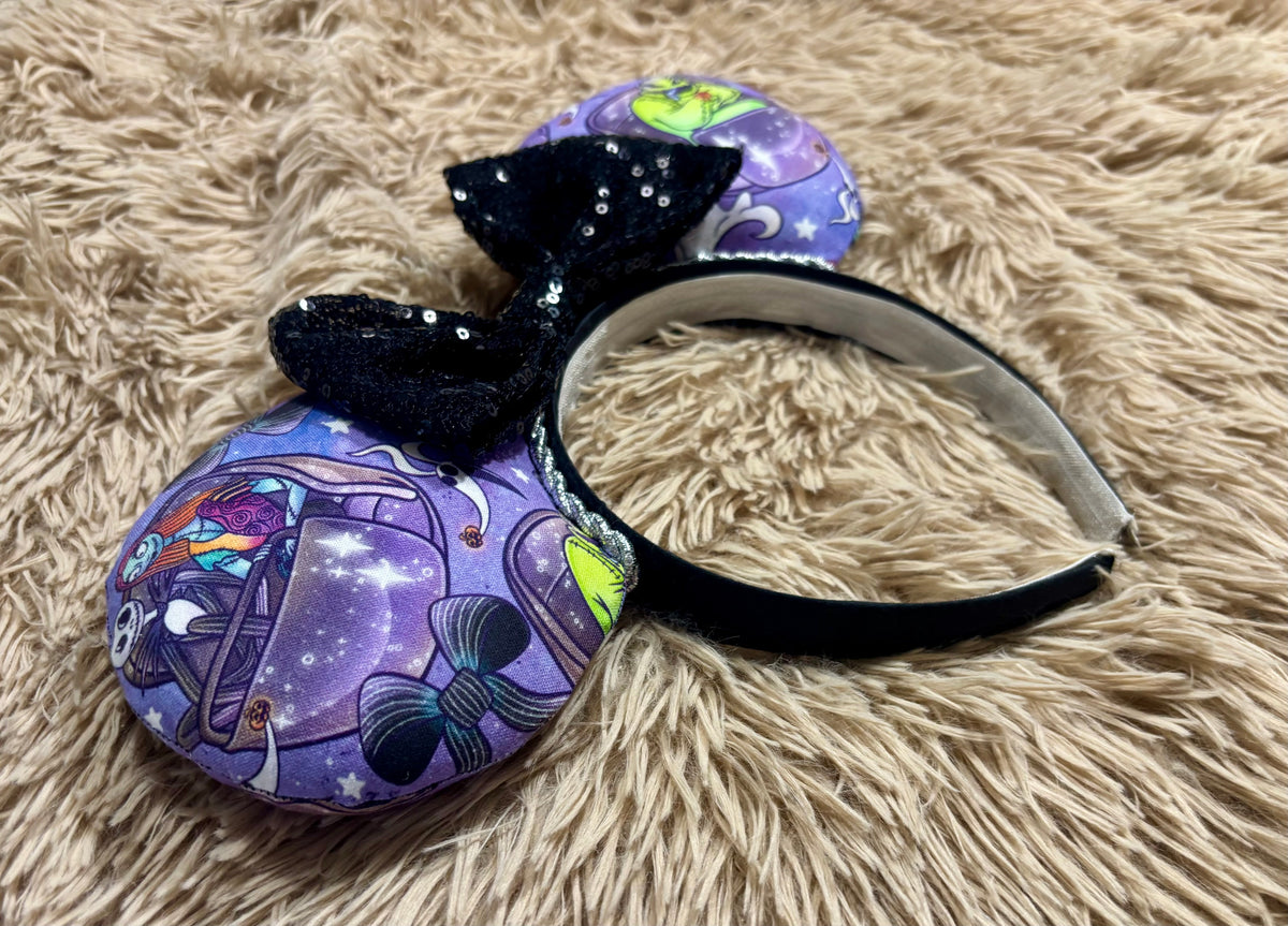 An ear headband accessory with a black sequined bow, featuring a purple HM and NBC themed print with a cartoon character in a buggy.
