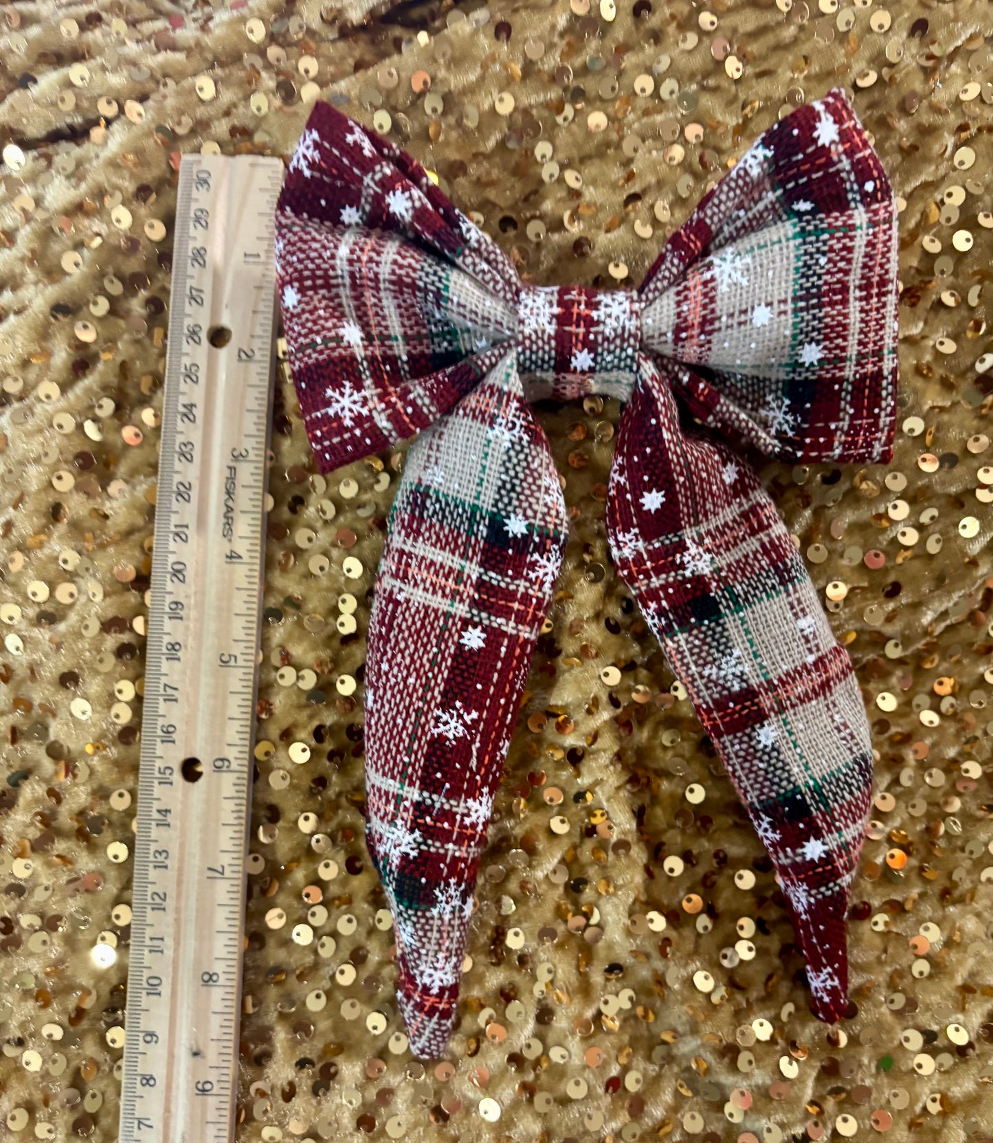 Plaid bow with sequins on a gold sequin background, next to a ruler for scale.
