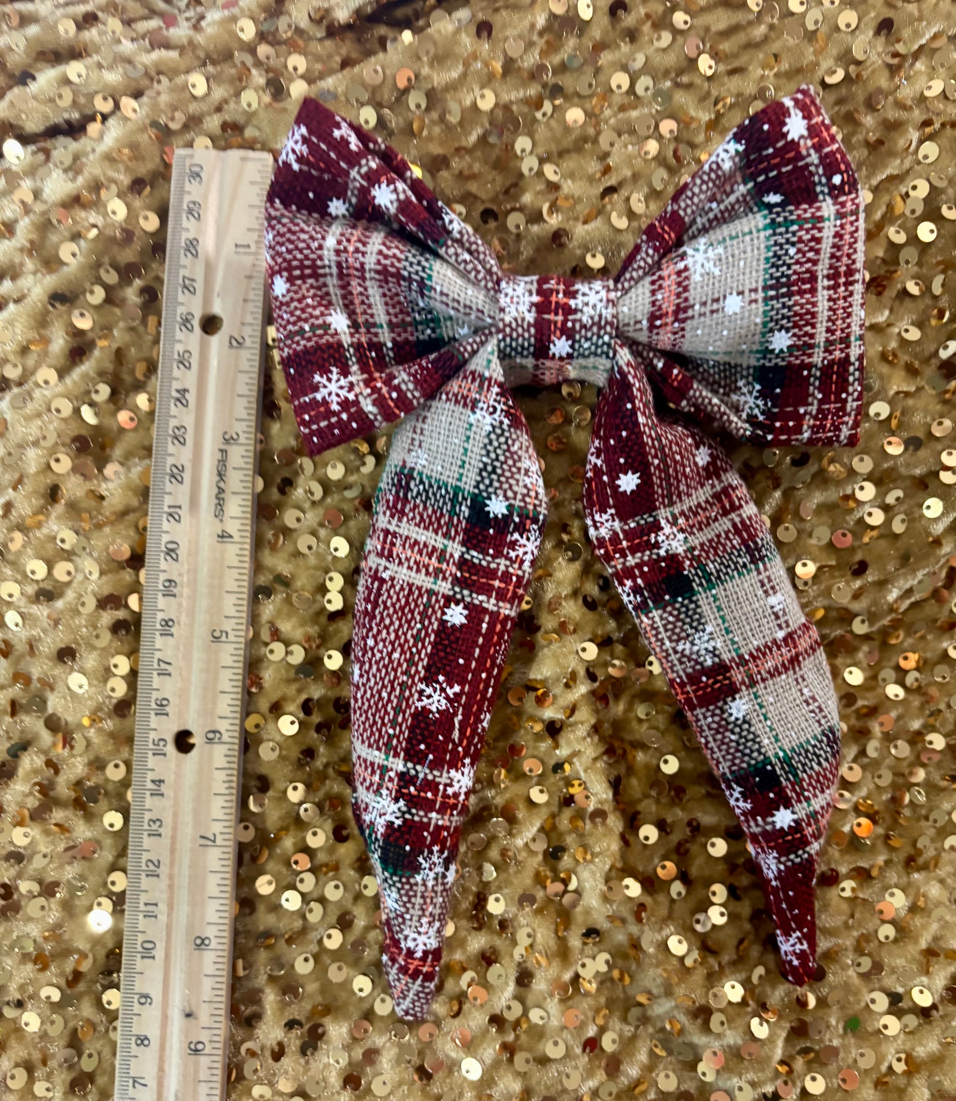 Plaid bow with sequins on a gold sequin background, next to a ruler for scale.