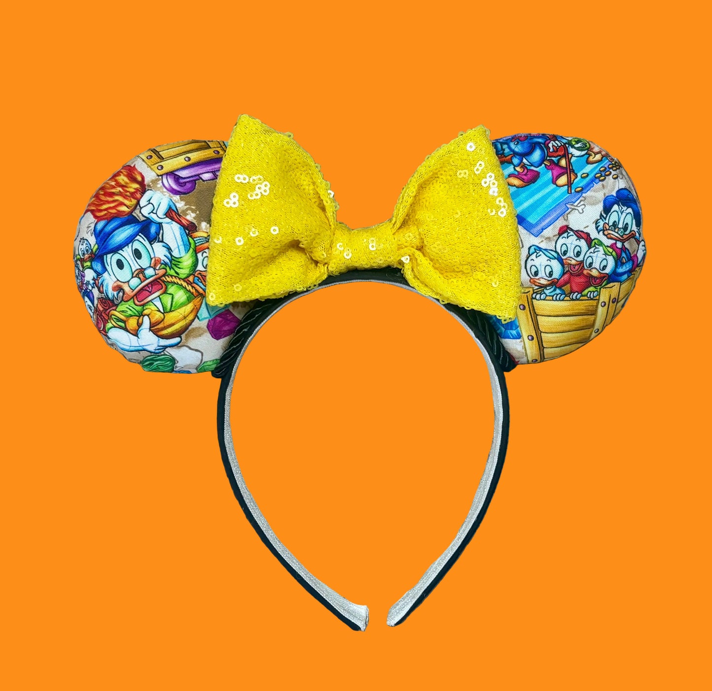 A headband featuring a colorful cartoon print of famous cartoon Duck characters, accented by a large yellow sequined bow in the center.