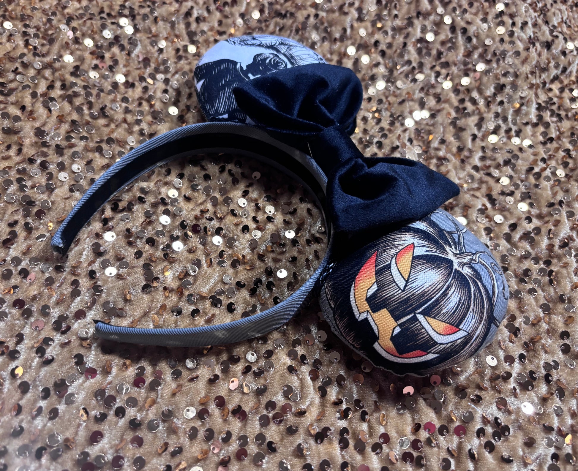 Handmade and one of a kind Halloween mouse ears with the fabric on both the front and back. Skeleton ghost having a seance on one side and an evil pumpkin on the other ear. The headband is grey and universal sized and fits most. The set has a black velvet bow. Item is shown on a gold sequin background.