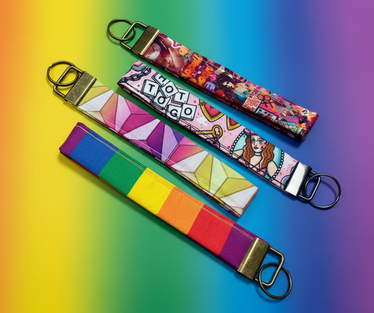 Two colorful keychains in different rainbow prints and two inspired by Chappell on them. Shown on a gradient background