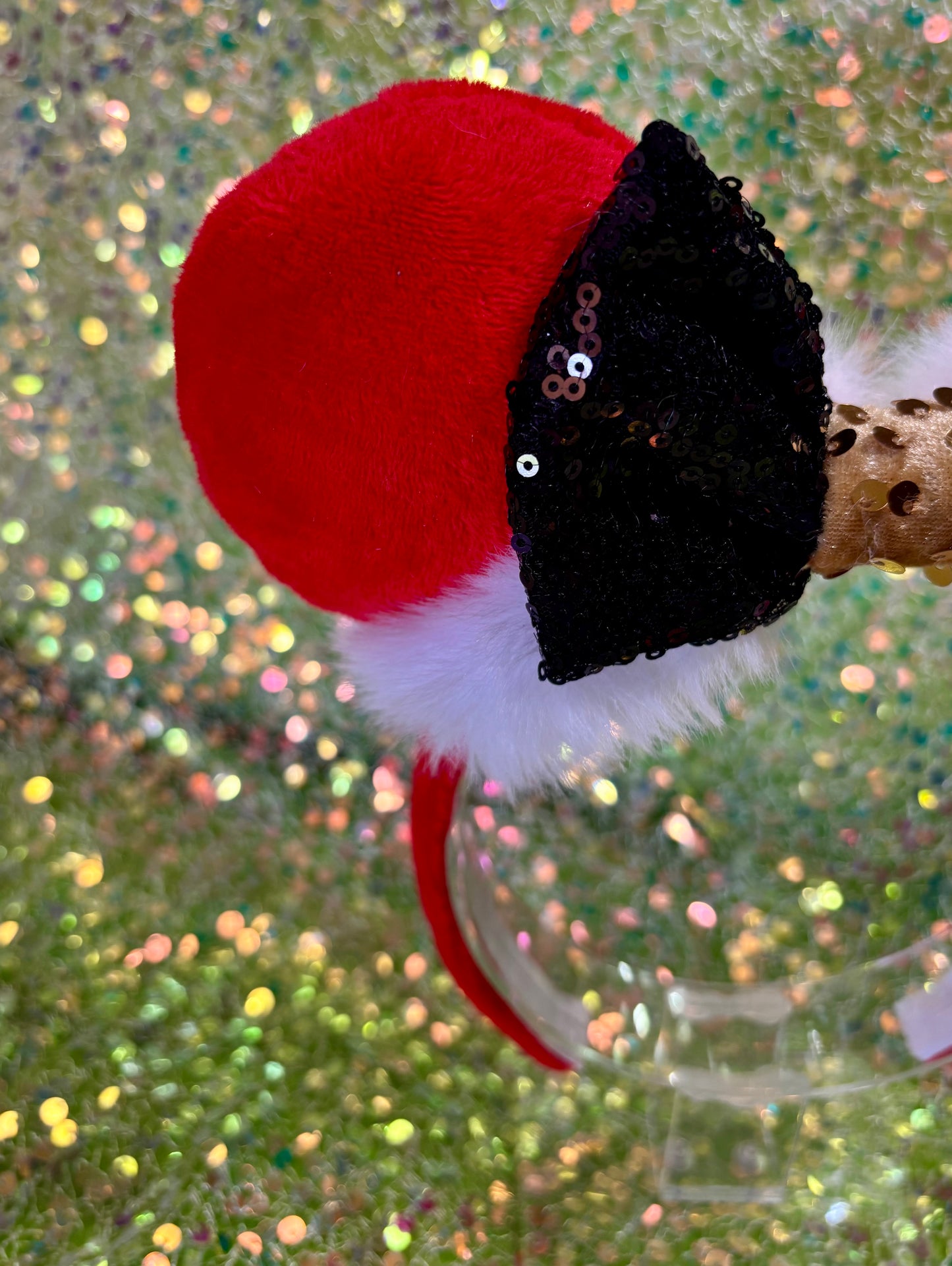 Minnie Mouse ears headband with red plush ears and black bow with gold middle and fluffy white trim on a glitter background