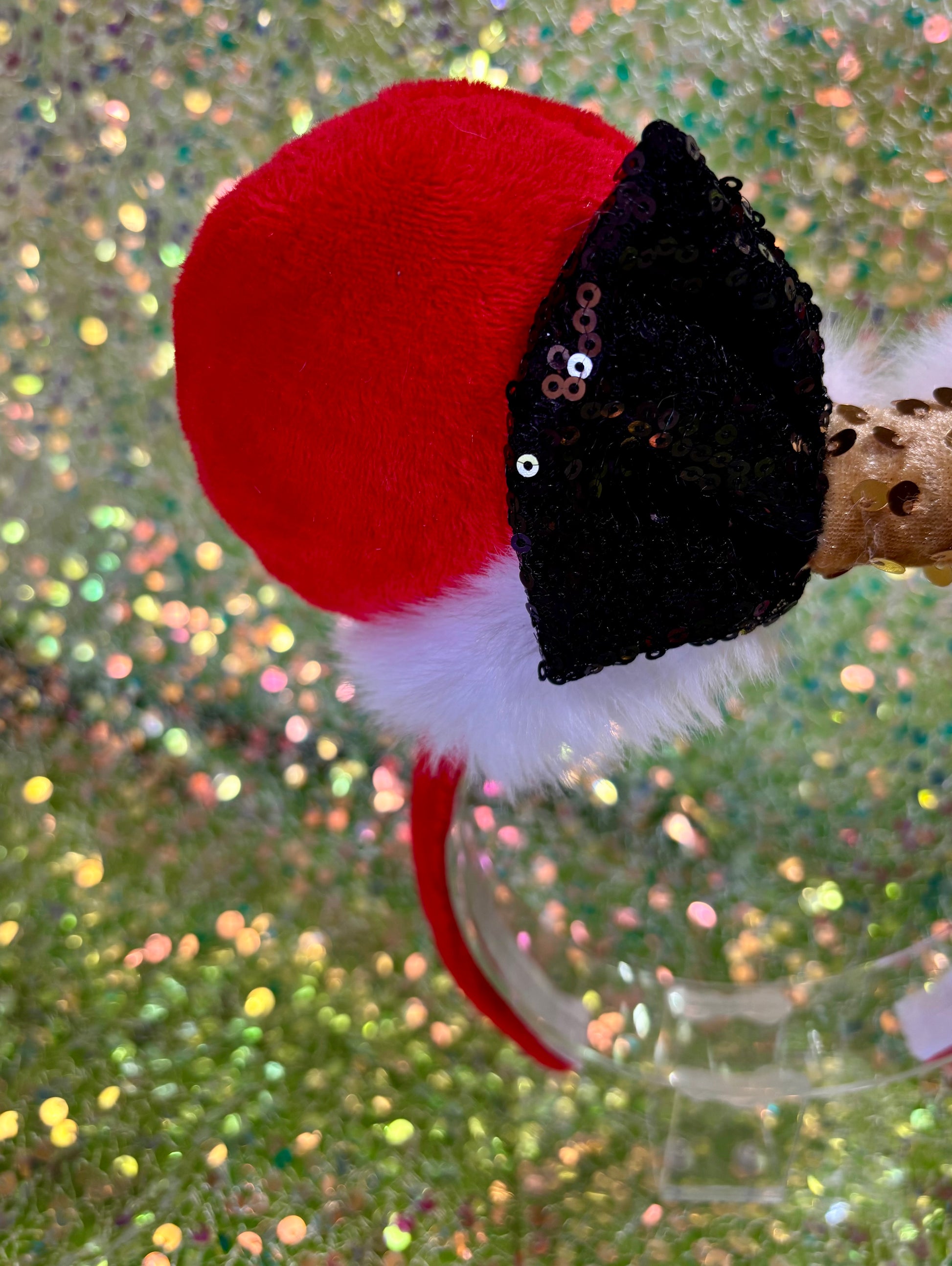 Minnie Mouse ears headband with red plush ears and black bow with gold middle and fluffy white trim on a glitter background