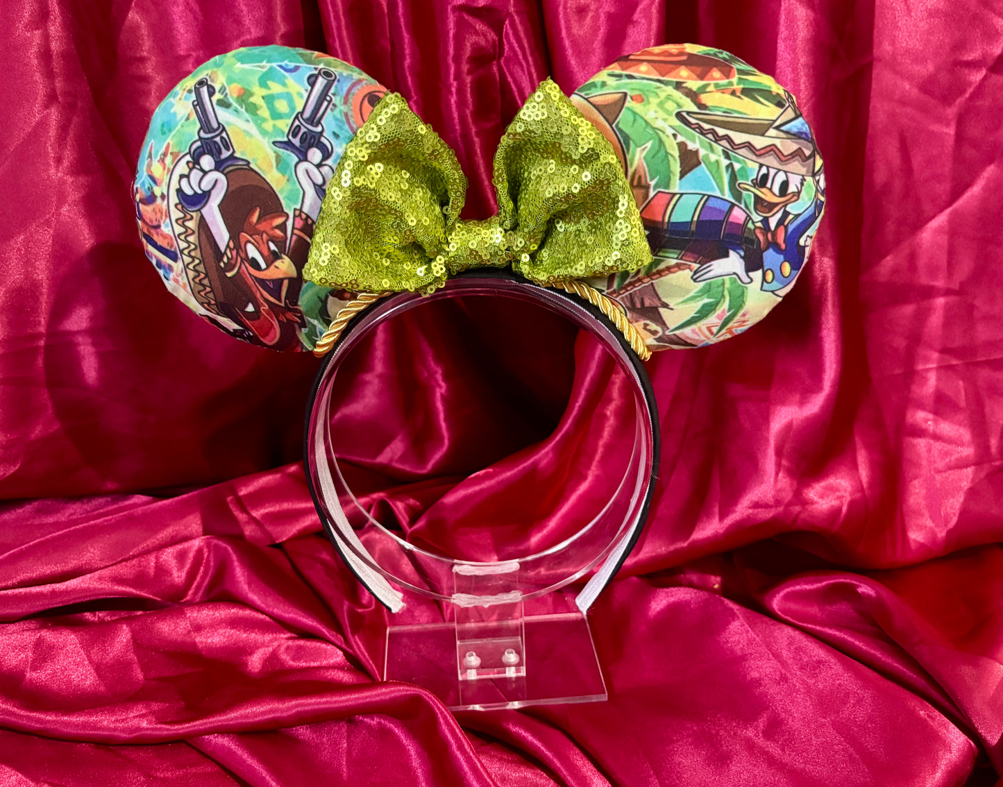 Colorful Handmade and ready to ship mouse ears with a green bow on a red satin background with duck cartoon images on the ears