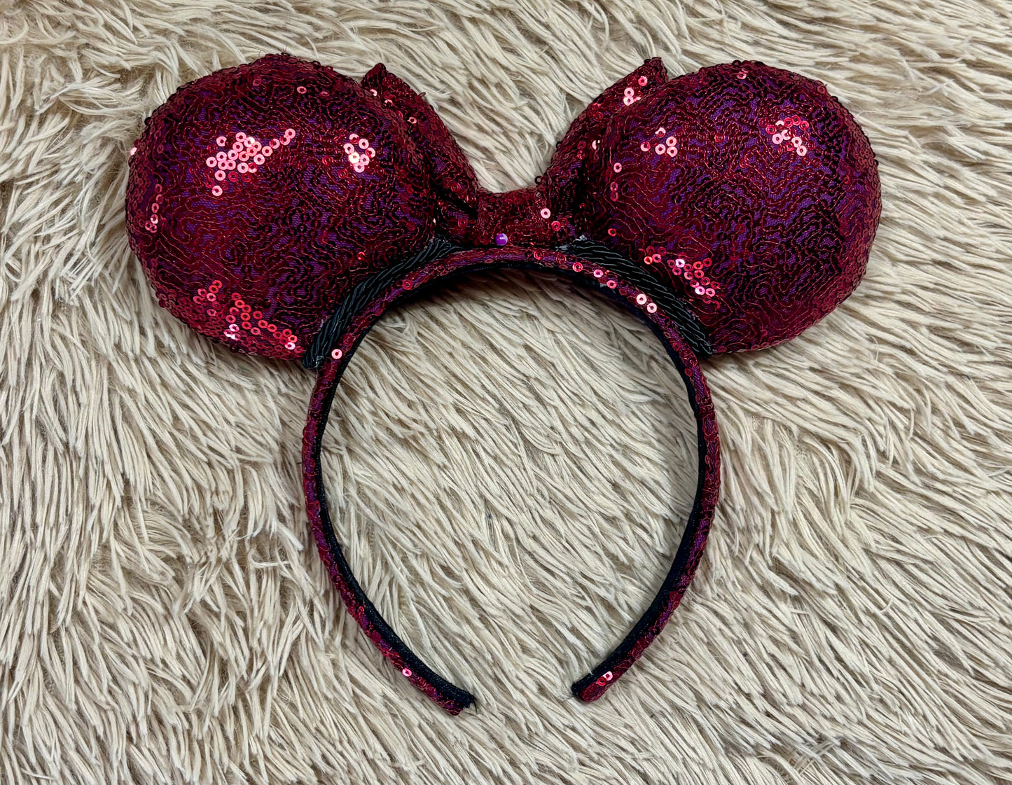 A pair of sequined ears headband with a bow, featuring deep magenta sequins on a black headband.