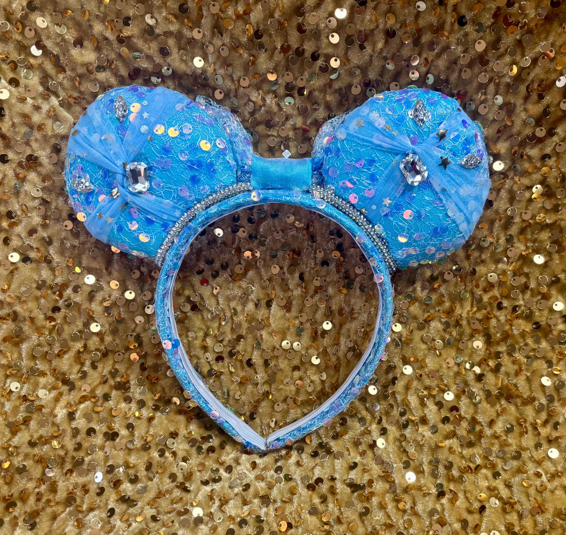 View from the back side of ears. Handmade and ready to ship blue sequin mouse ears headband inspired by Cinderella with tulle and silver gemstones with a crown charm middle and rhinestone trim along inner ears.