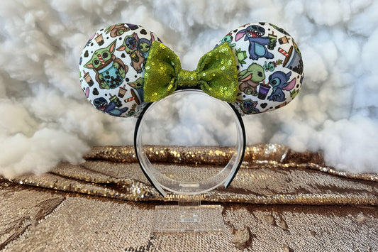 Coffee buddies Mouse ears with a green sequin bow. Shown on a stand against a textured background