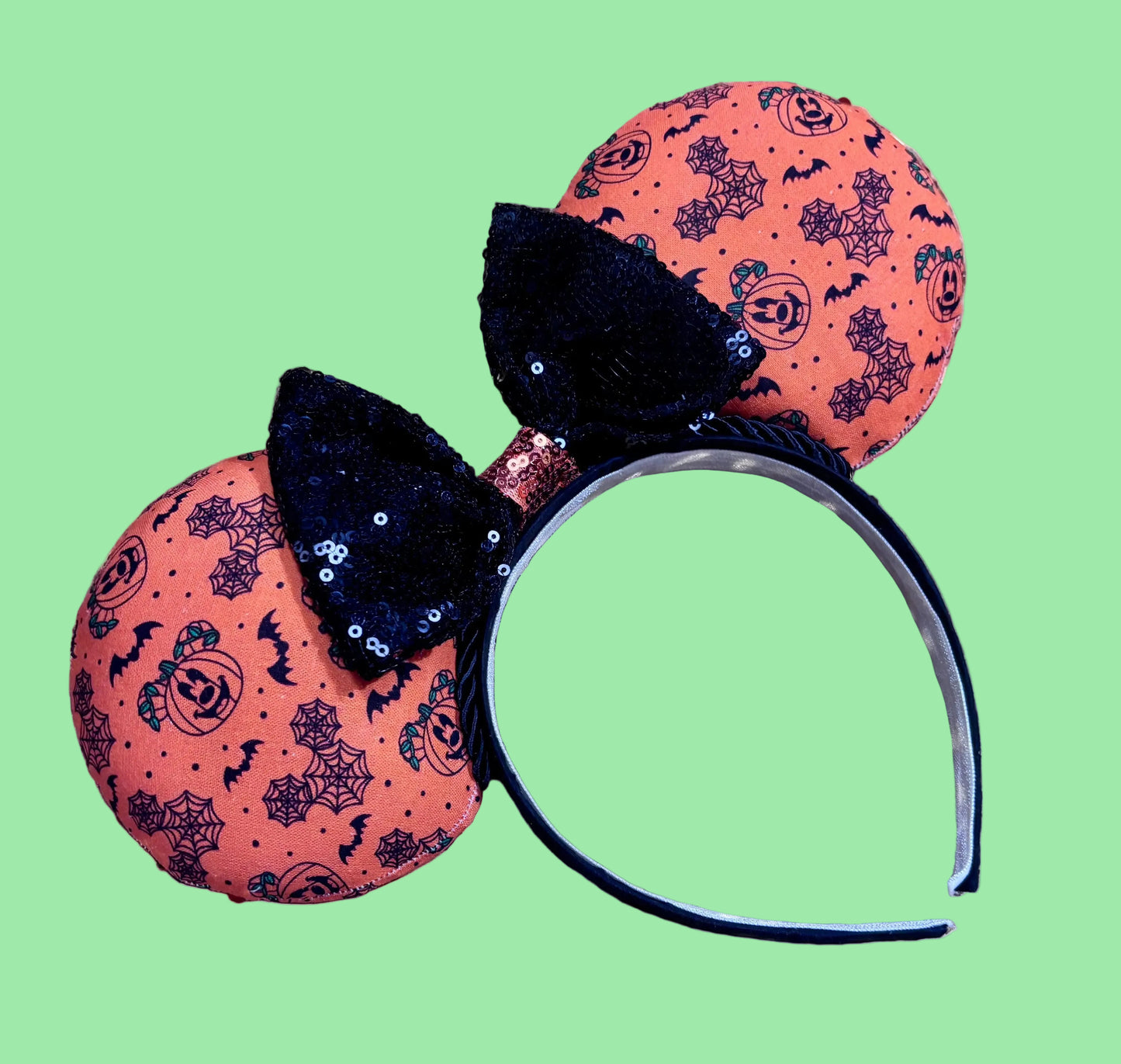 Halloween mouse ears with the fabric on both the front and back. It's orange with bats, mouse shaped pumpkins and spider webs. The headband is black universal sized and fits most. The set has a black with orange middle sequin bow. Item is shown on a white background.