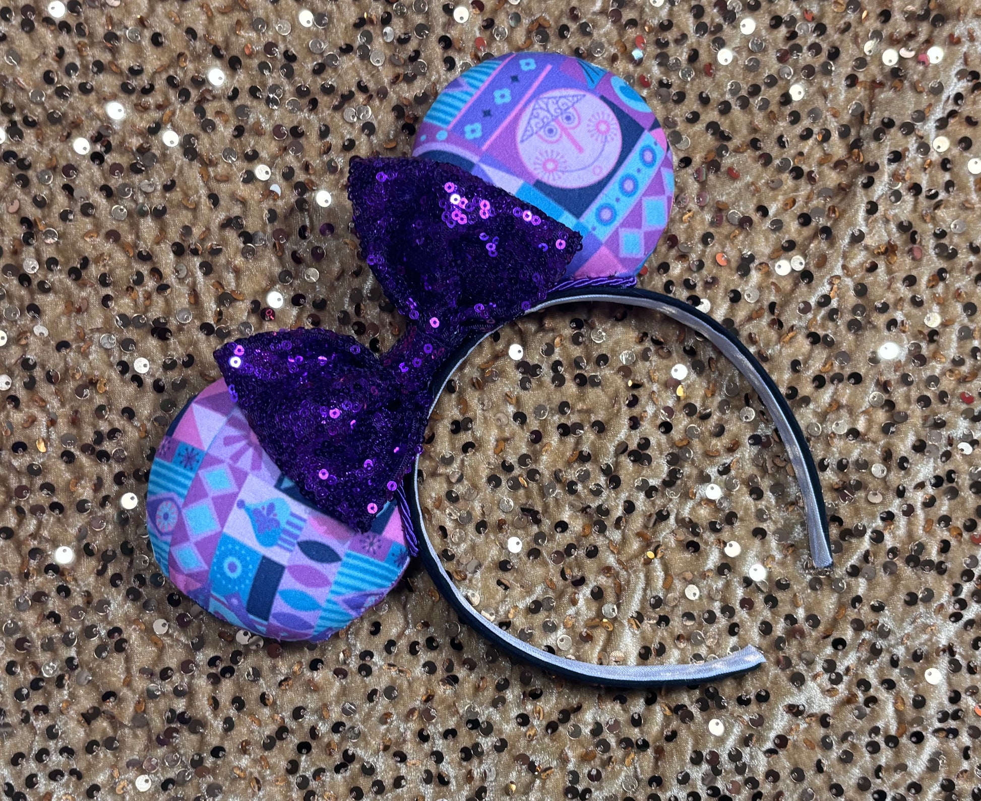 Decorative headband with purple bow and patterned design on a glittery background