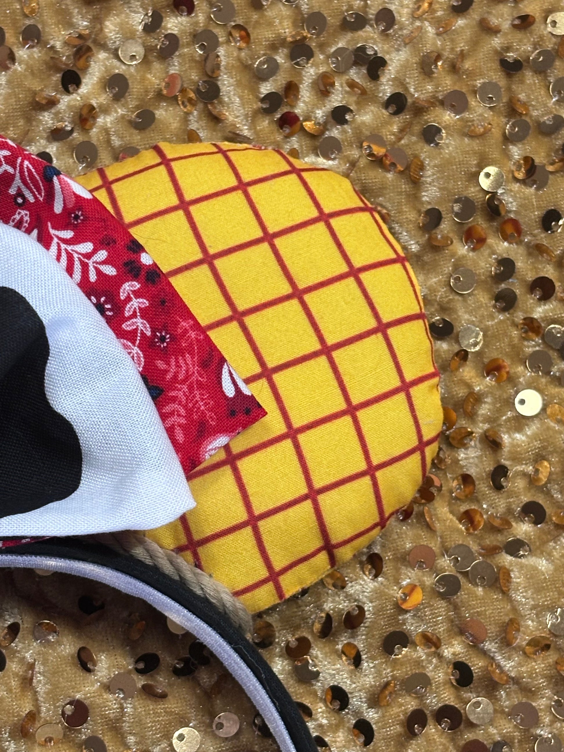 Handmade and ready to ship. Sheriff Woody Inspired mouse ears with the fabric on both the front and back that looks like his shirt. The fabric on the headband is black and is universal sized and fits most. The set has a bandana and cow print layered bow with brown trim along the inner ears to look like rope. Item is shown on a white background.