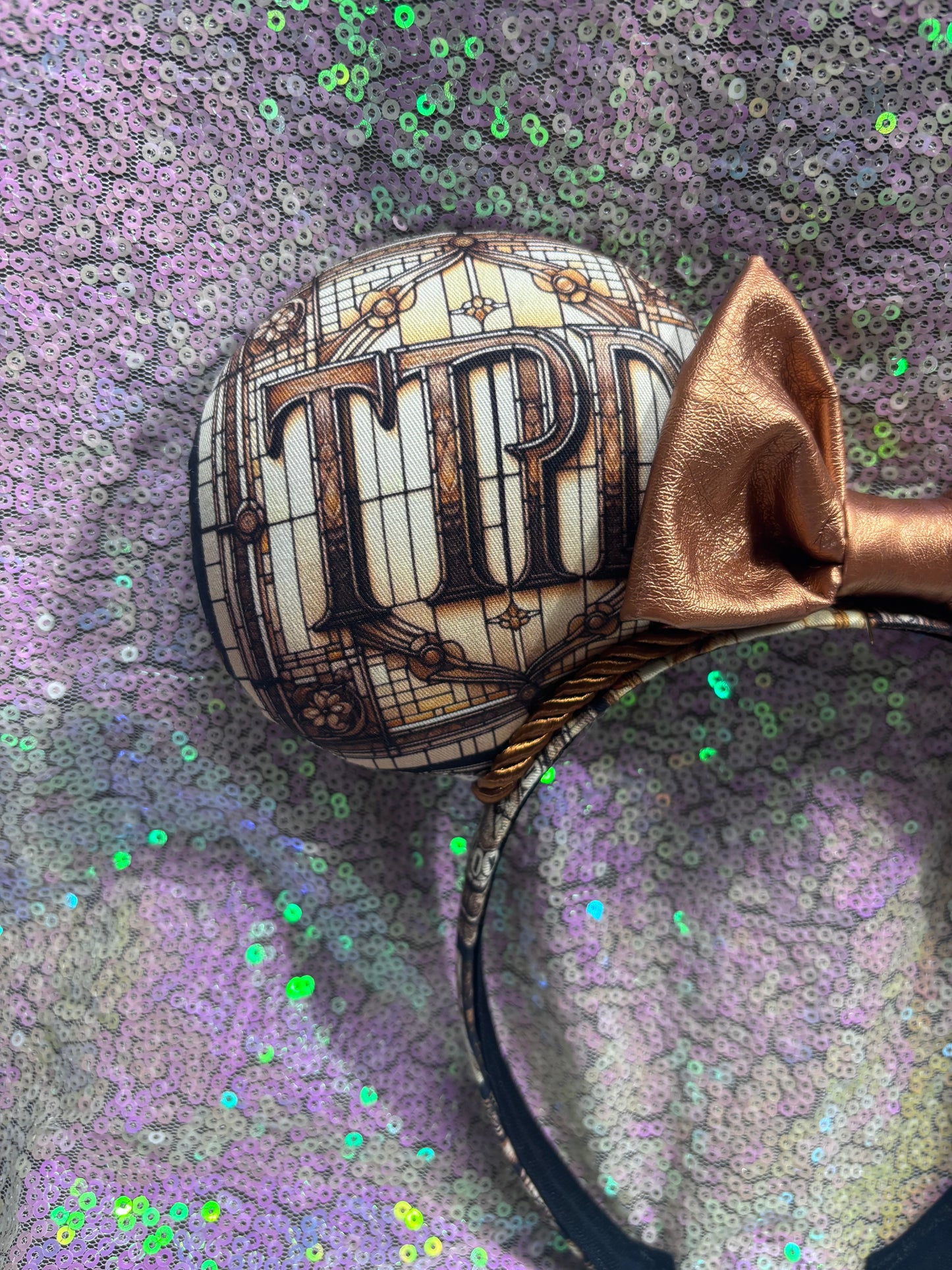 Mouse ears with a rose gold pleather bow and decorative elements on a textured purple background